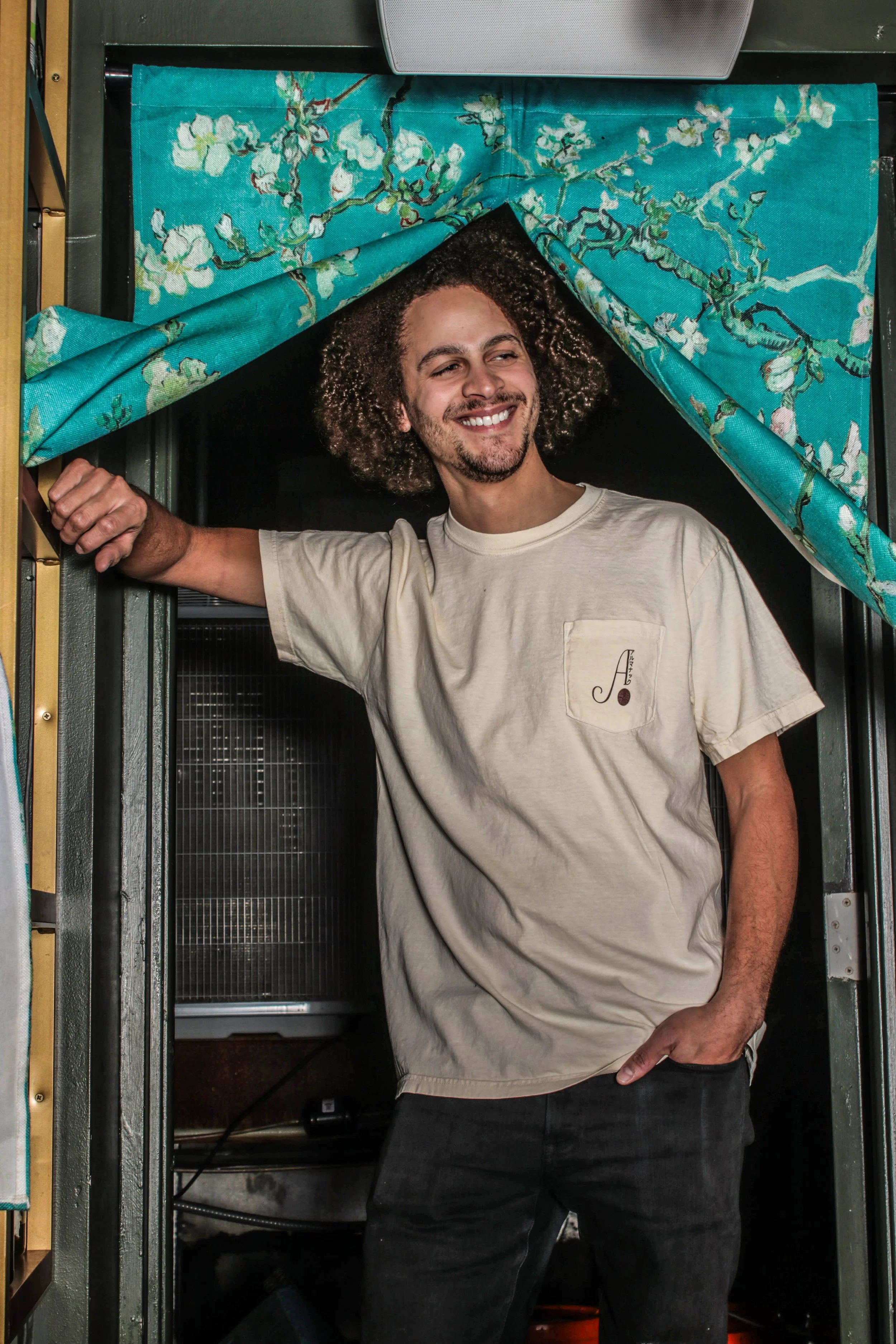 man smiling walking through curtain in cream almanac tee shirt