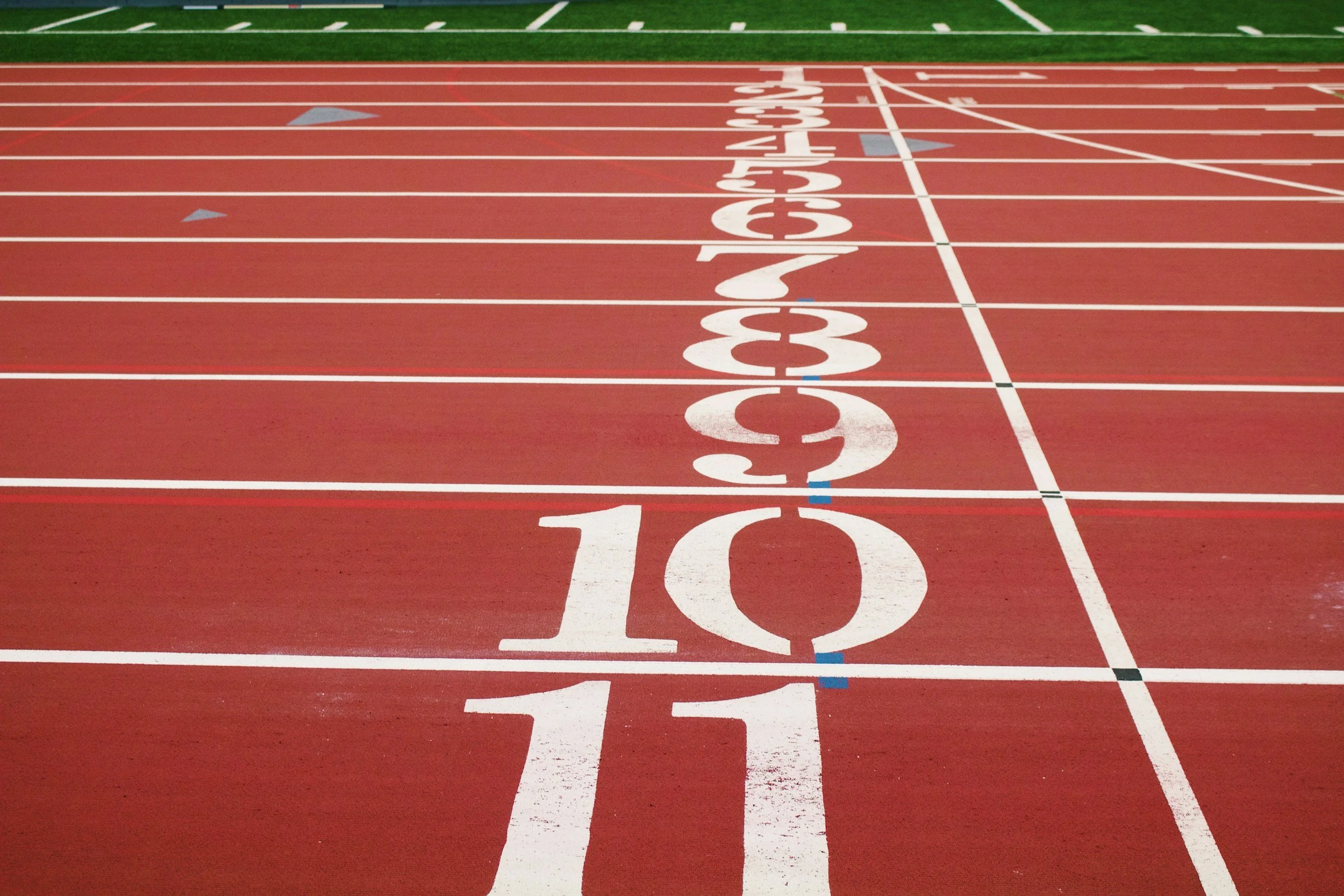 Close-up view of a red running track with lane markings and the starting line, featuring large white numbers 10, 11, 12, etc.