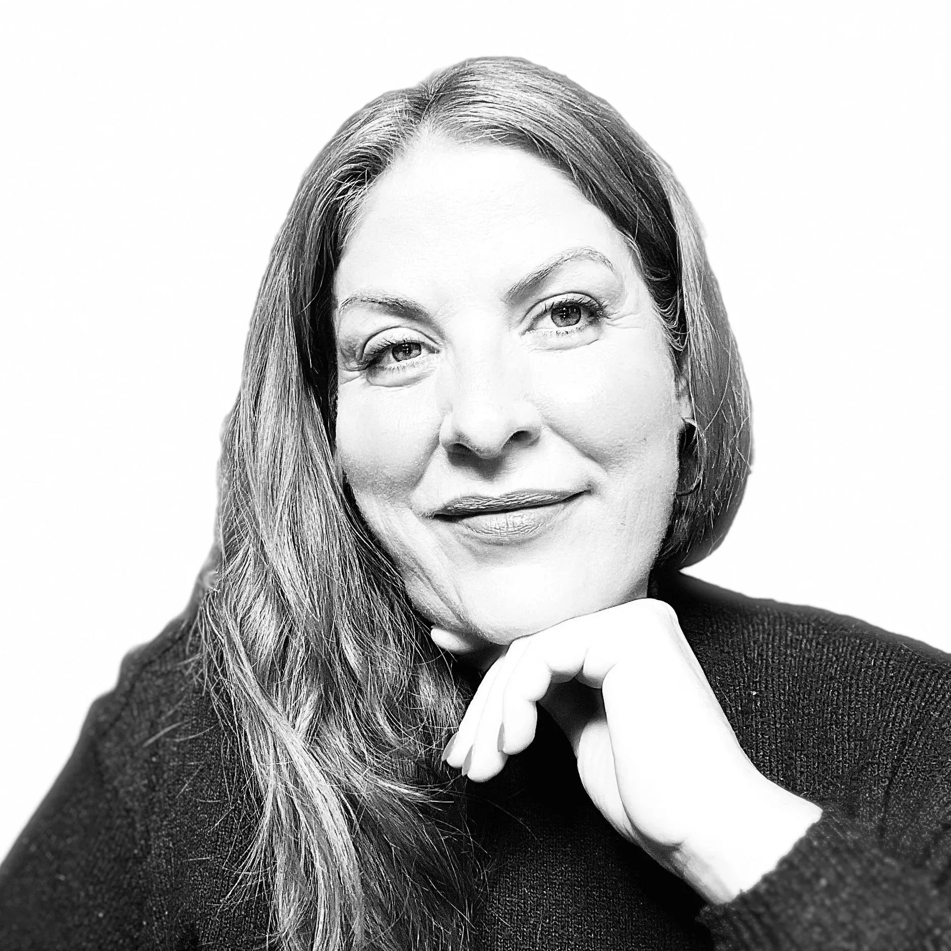 Black and white portrait of a woman with long hair, resting her chin on her hand, smiling softly.