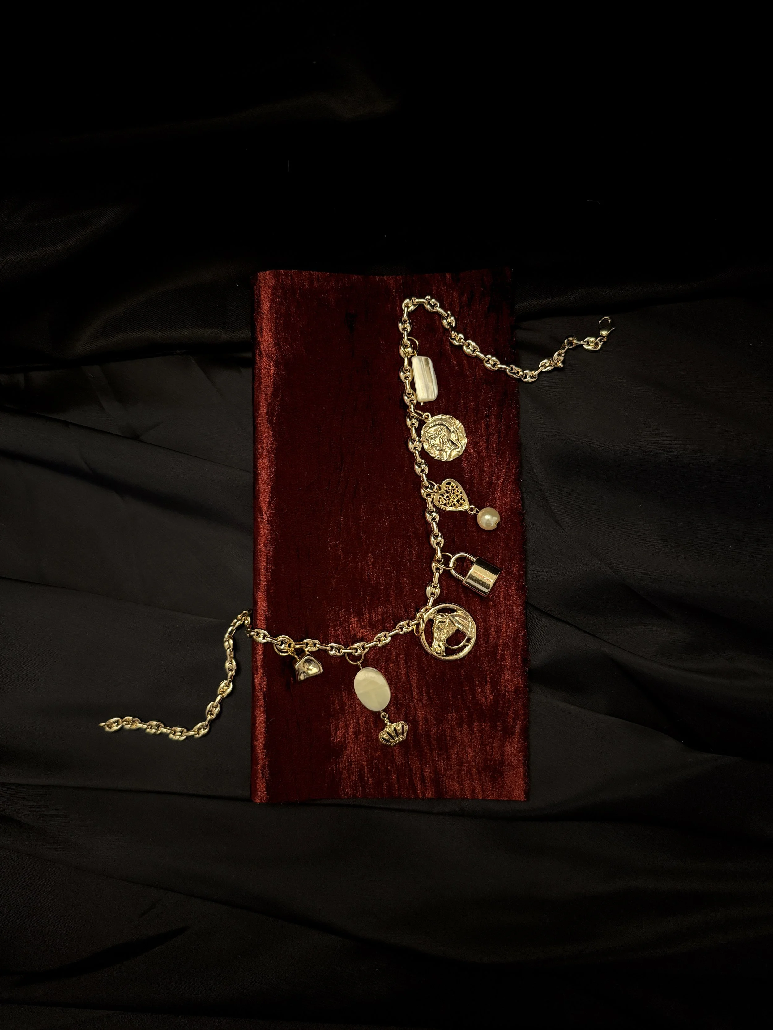 Gold charm bracelet with various charms, resting on a red velvet display against a black background.