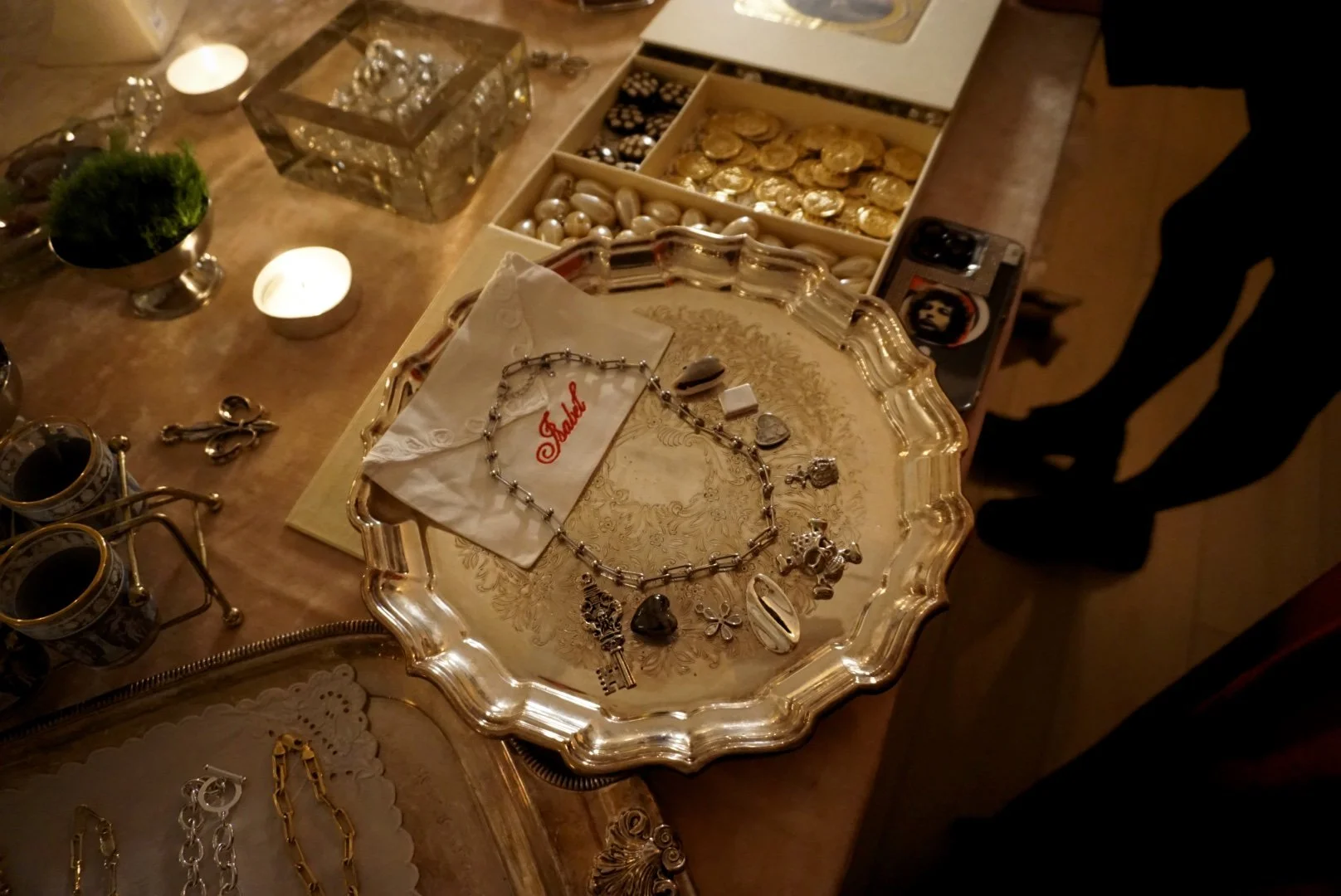 A jewelry display table with various necklaces, earrings, and rings, along with a box of chocolates, lit candles, and other decorative items.