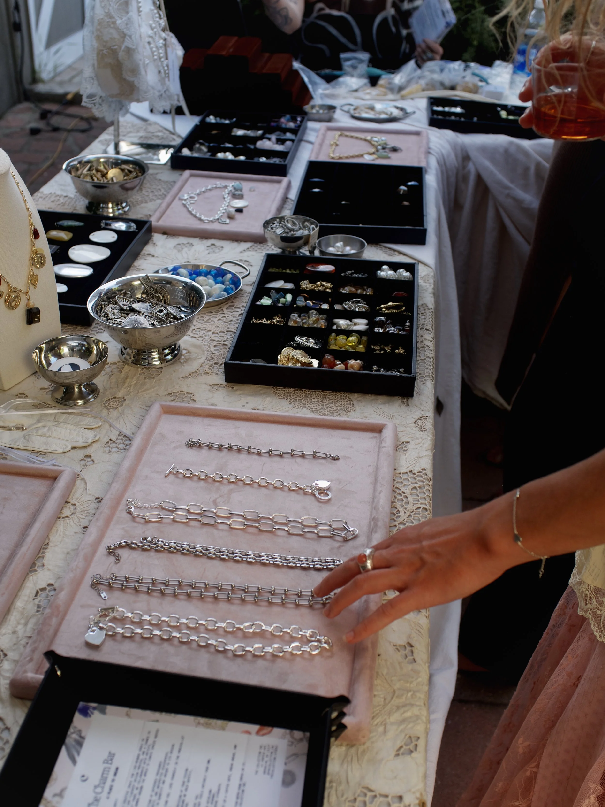 A display of silver jewelry, including bracelets and necklaces, on a pink velvet tray at an outdoor market or jewelry sale.