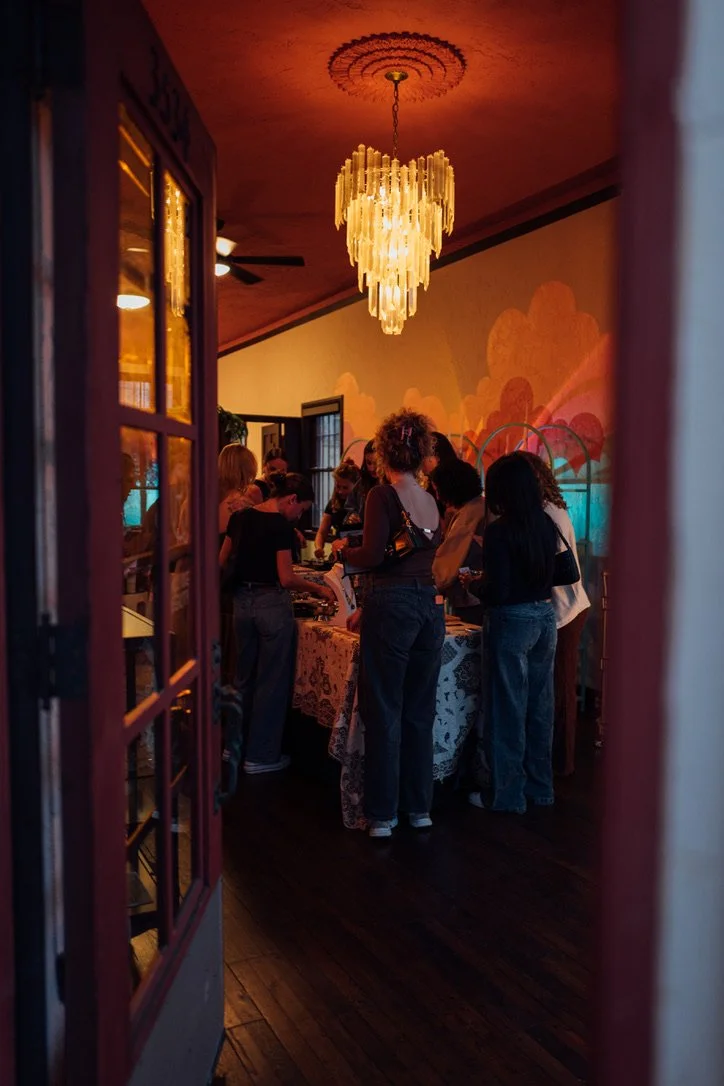 People gathered around a table in a dimly lit room with a colorful wall mural and a chandelier hanging from the ceiling.