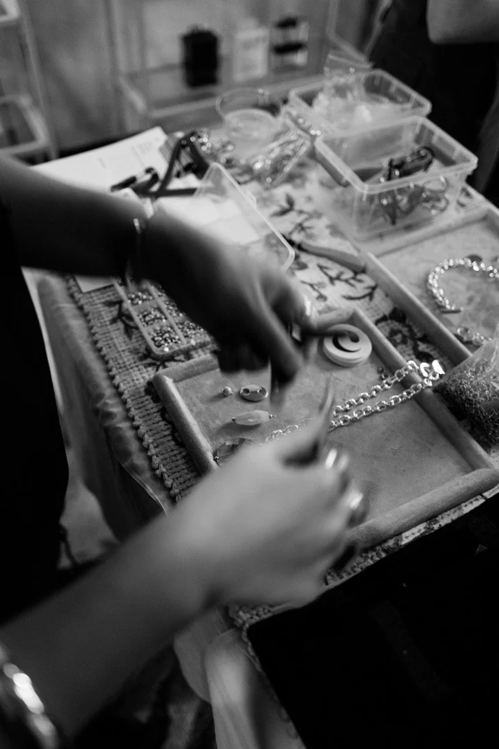 Close-up of hands arranging jewelry on a table with various jewelry pieces and tools.