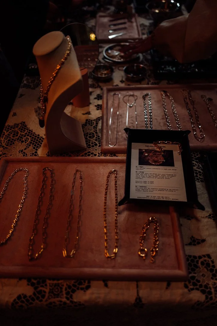 Jewelry display table with necklaces and bracelets, including a jewelry stand and a framed informational sign, at a store or market.