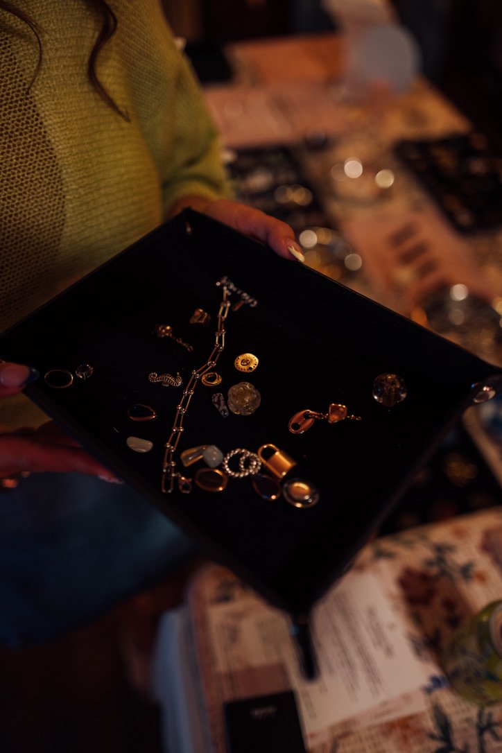 Person holding an open jewelry box with various rings, necklaces, and earrings inside, in a dimly lit environment.