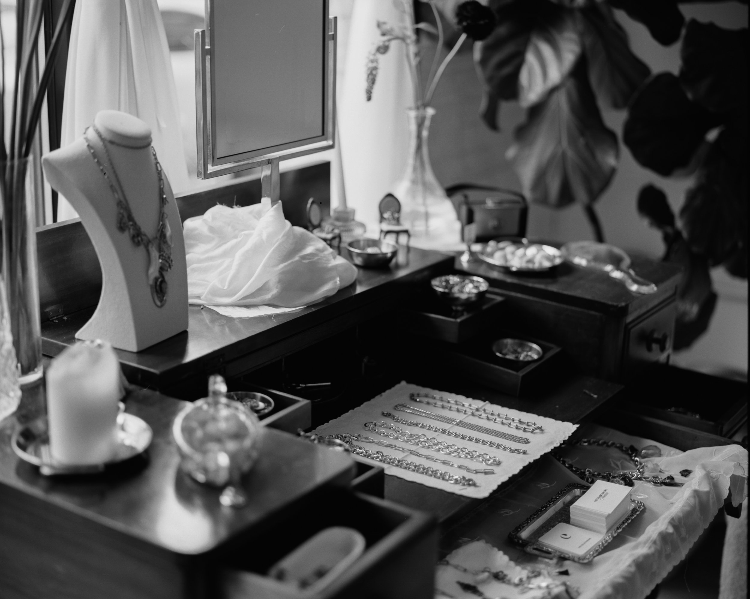 A jewelry display table with various necklaces, bracelets, and rings, featuring a jewelry bust with a necklace, a mirror, and decorative items, in a black and white photo.