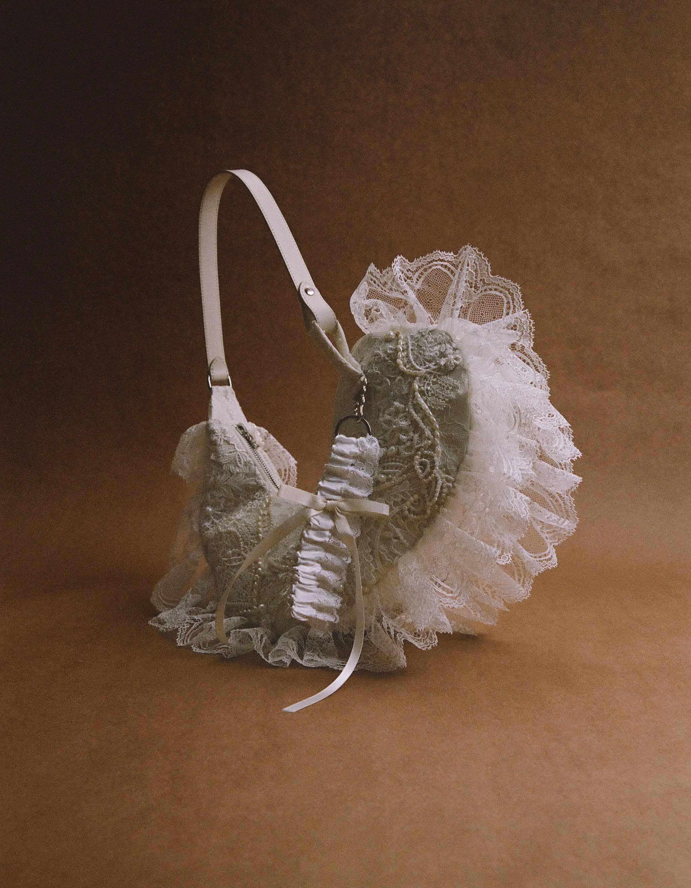 A lace lingerie bag with a ruffled lace edge and a satin ribbon, containing a small matching lace pouch, set against a brown background.