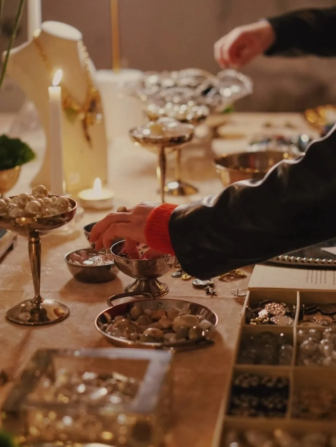 Close-up of a person shopping for jewelry at a display table with various silver and gold jewelry pieces and ornaments, illuminated by warm lighting.