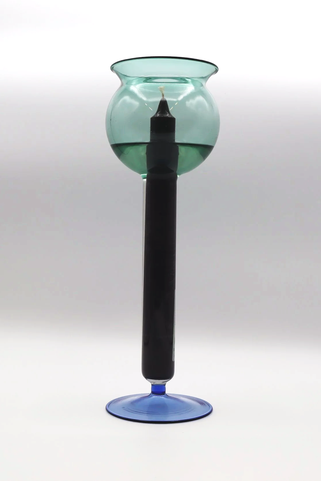 Candelabro di vetro con candela accesa, uno strano oggetto artistico con base in vetro blu e supporto nero, sfondo bianco