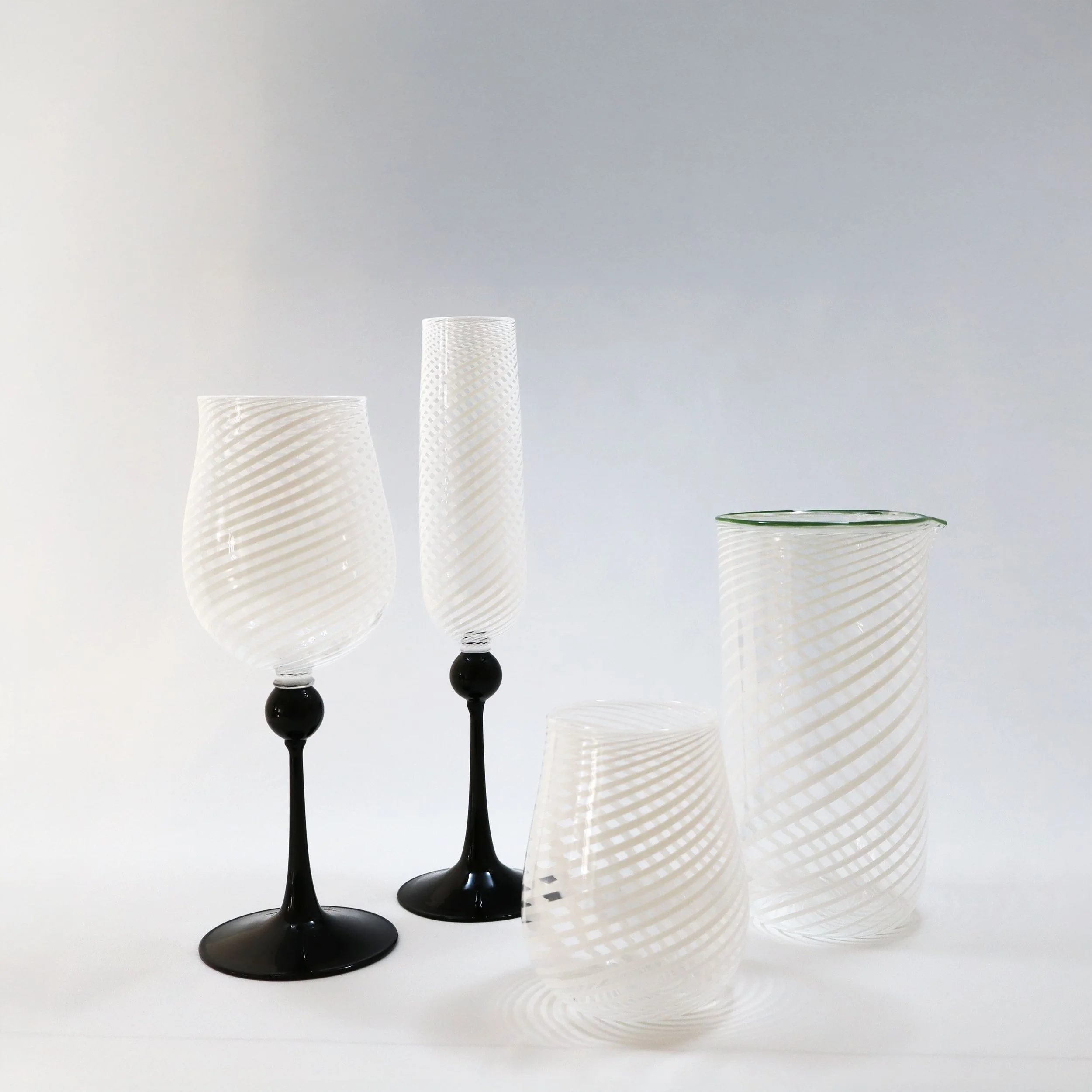 Set di quattro bicchieri di vetro trasparente con motivi a spirale, due con supporto nero, uno alto e sottile, uno più corto e rotondo, e due più grandi senza supporto.