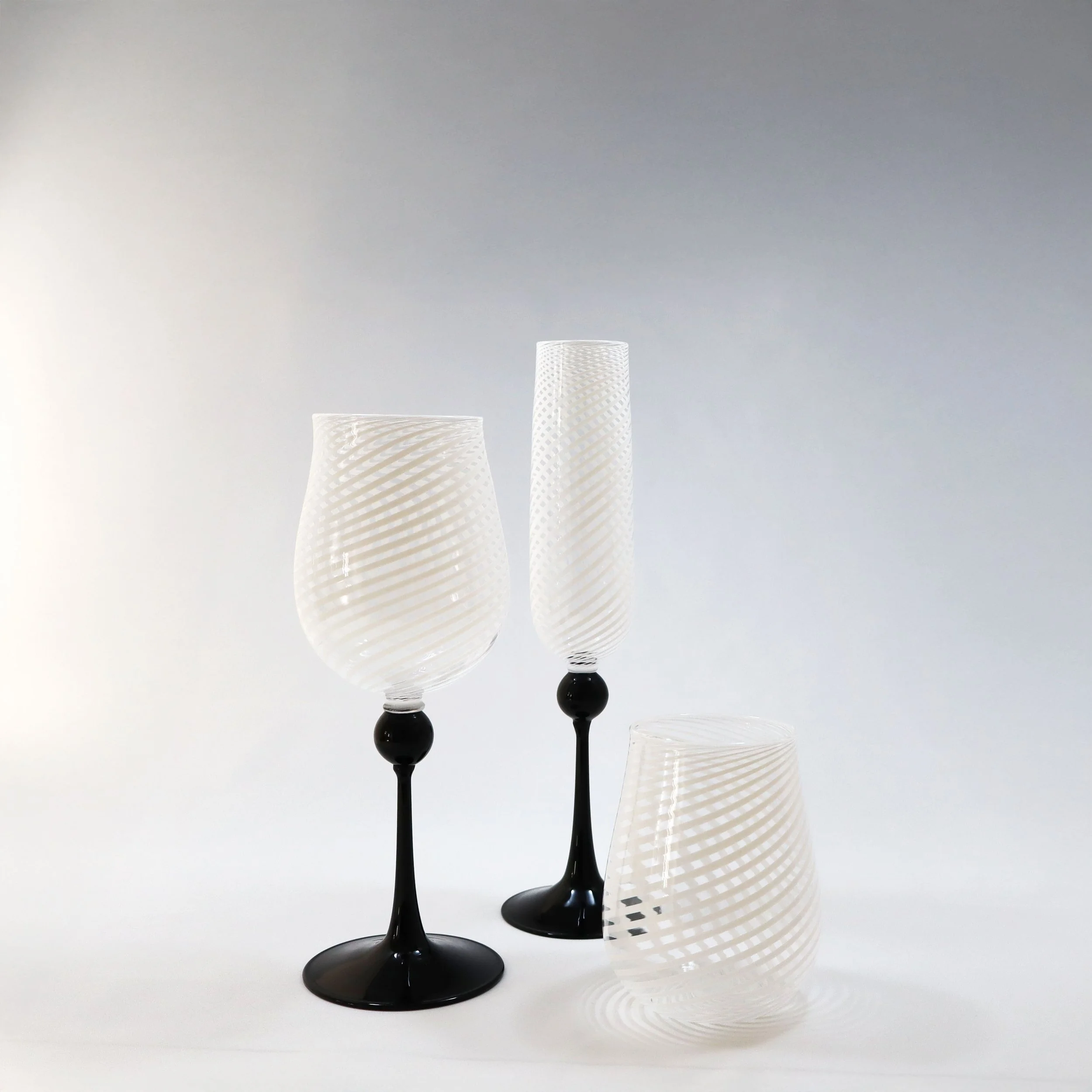 Tre bicchieri di vetro decorativi con motivi a spirale, due con basi nere e uno inclinato.