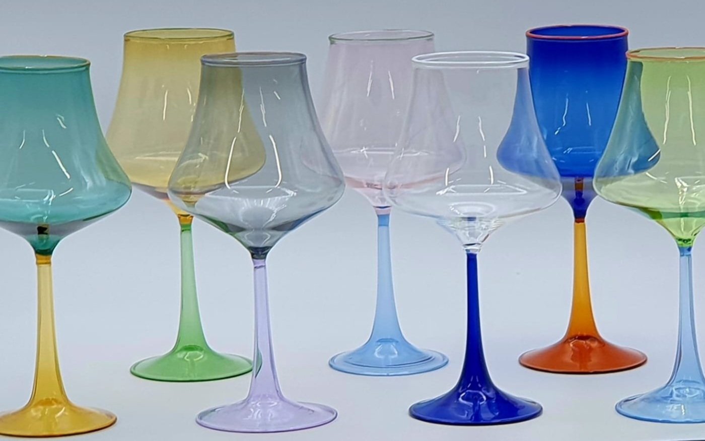 Set di bicchieri di vetro colorati trasparenti disposti in fila su una superficie bianca.