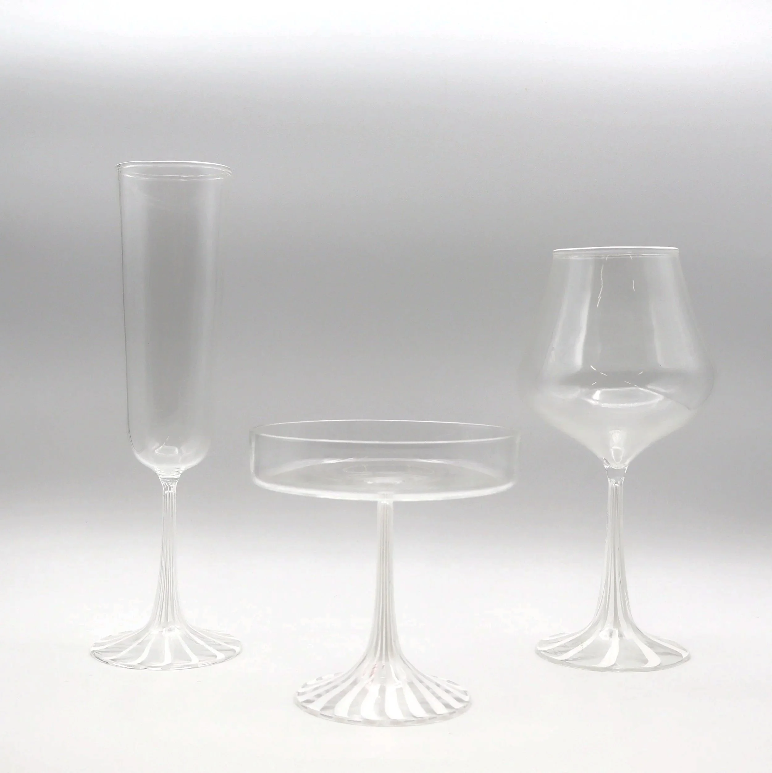 Tre bicchieri di cristallo trasparenti disposti su una superficie bianca.