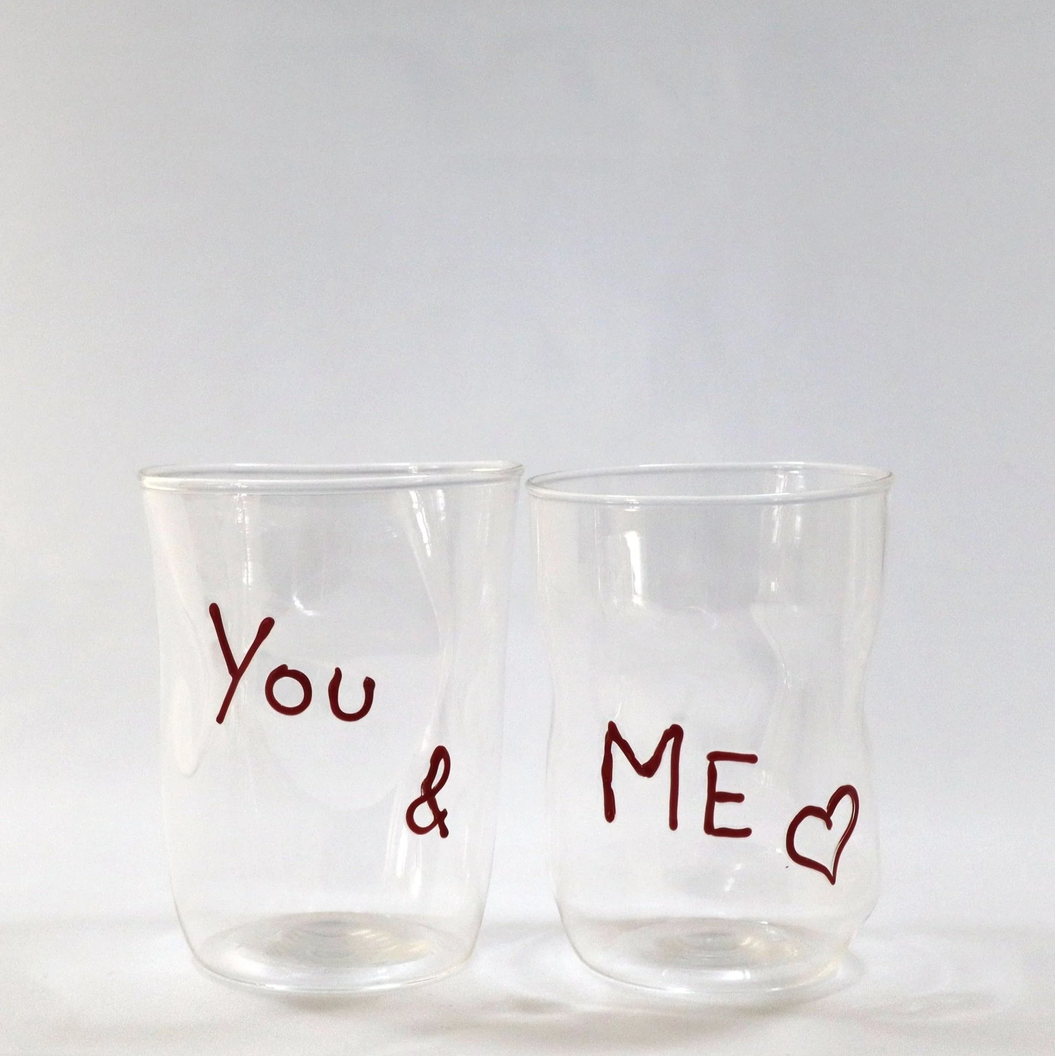 Due bicchieri di plastica trasparenti con scritte rosse, uno con 'You &' e l'altro con 'ME ♥'