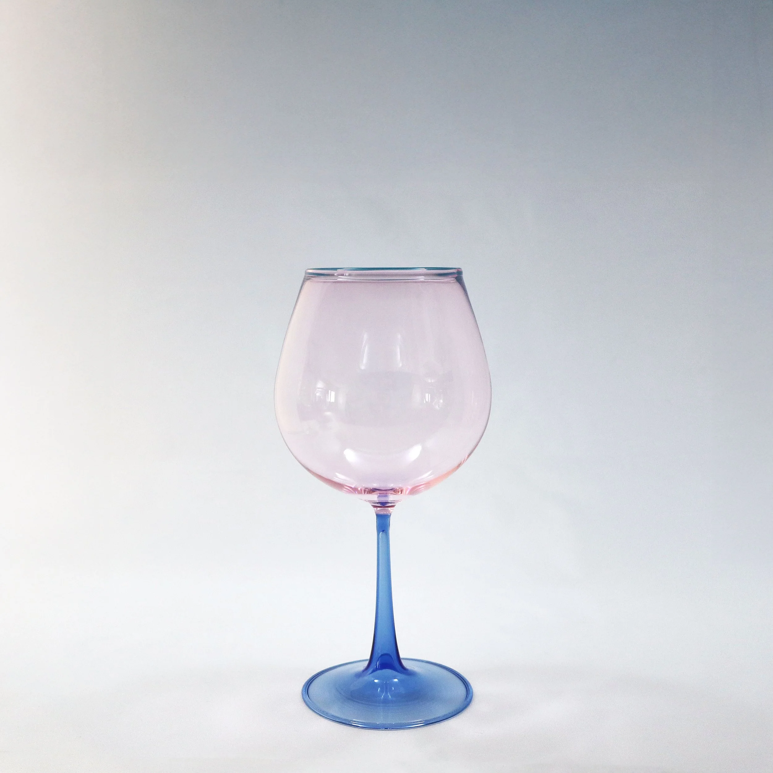 Vetro colorato rosa e blu con forma di calice su sfondo grigio chiaro.