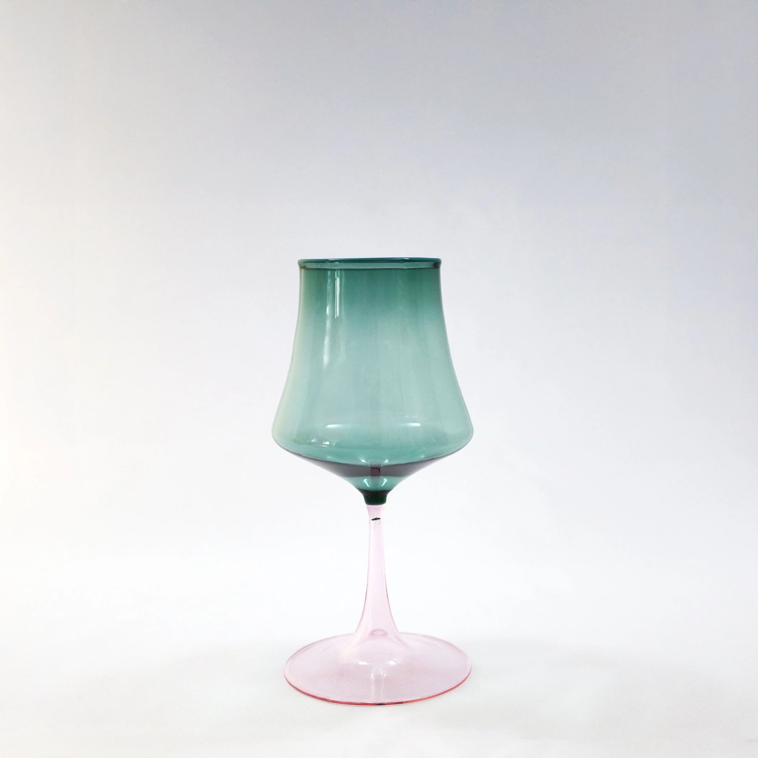 Bicchiere di vetro colorato con guscio sfumato dal rosa alla verde e forma elegante, su sfondo bianco.