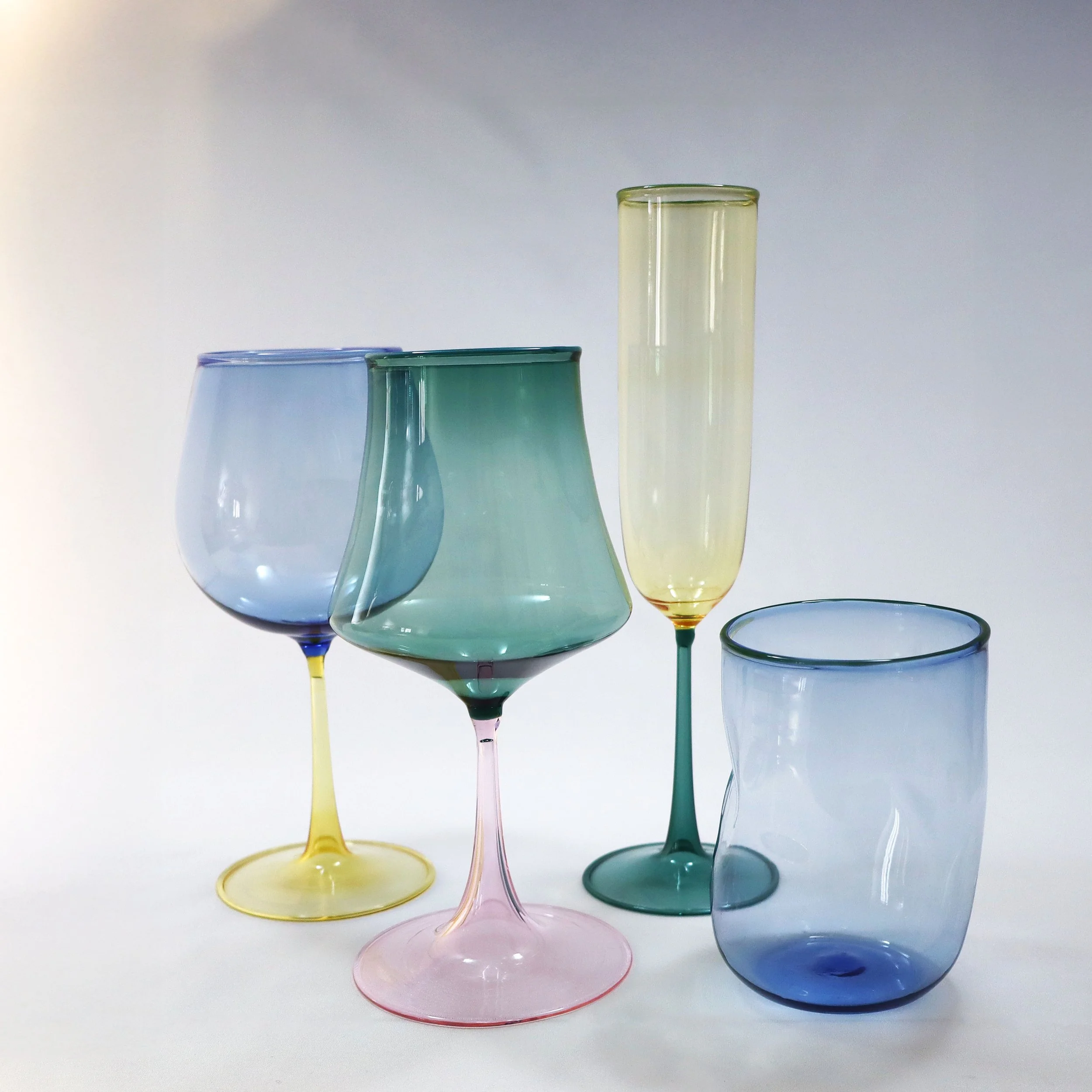Quattro bicchieri di diverso colore e forma disposti su uno sfondo bianco.