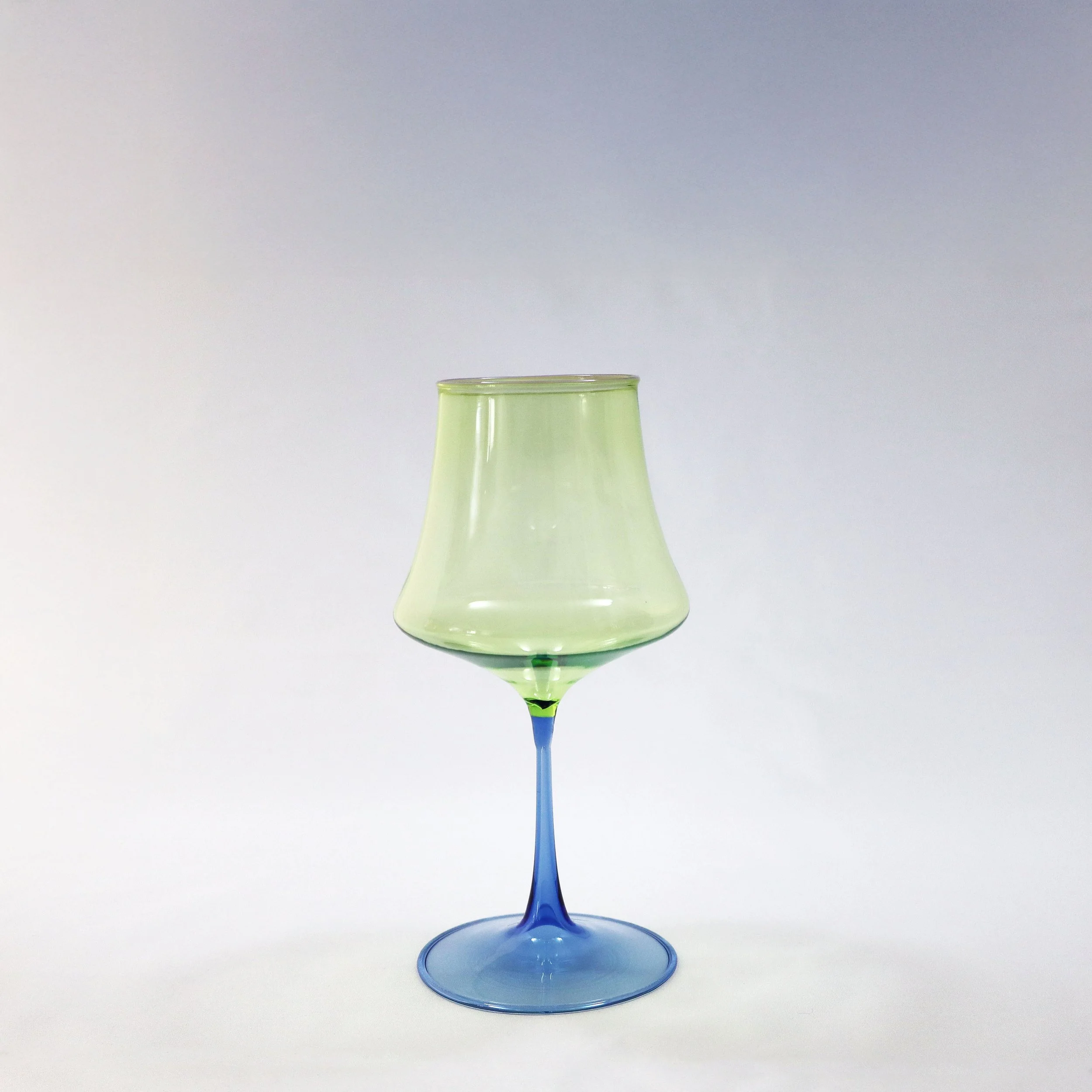 Calice di vetro colorato verde chiaro con stelo blu su sfondo bianco