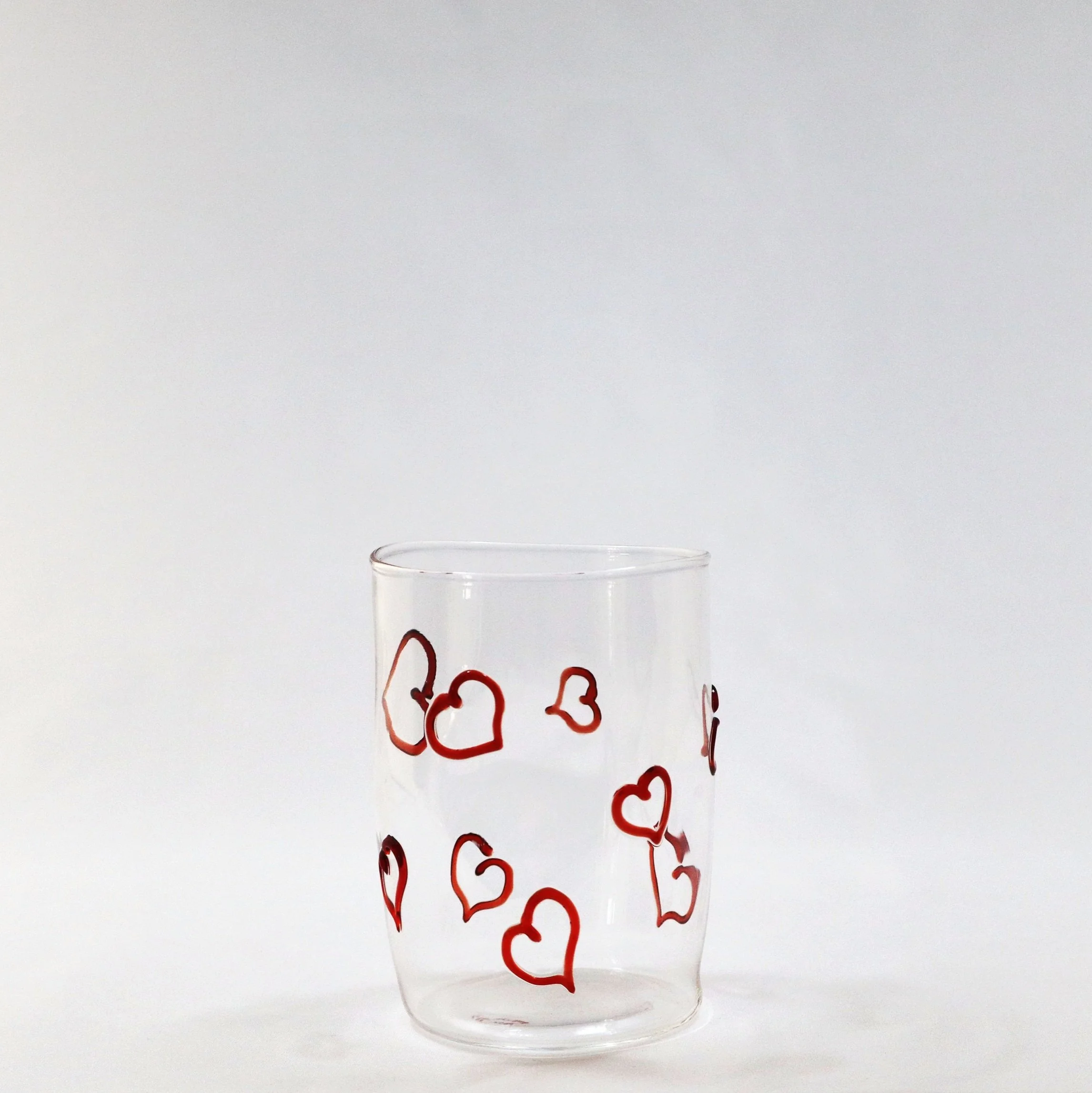 Bicchiere di vetro trasparente decorato con cuori rossi.
