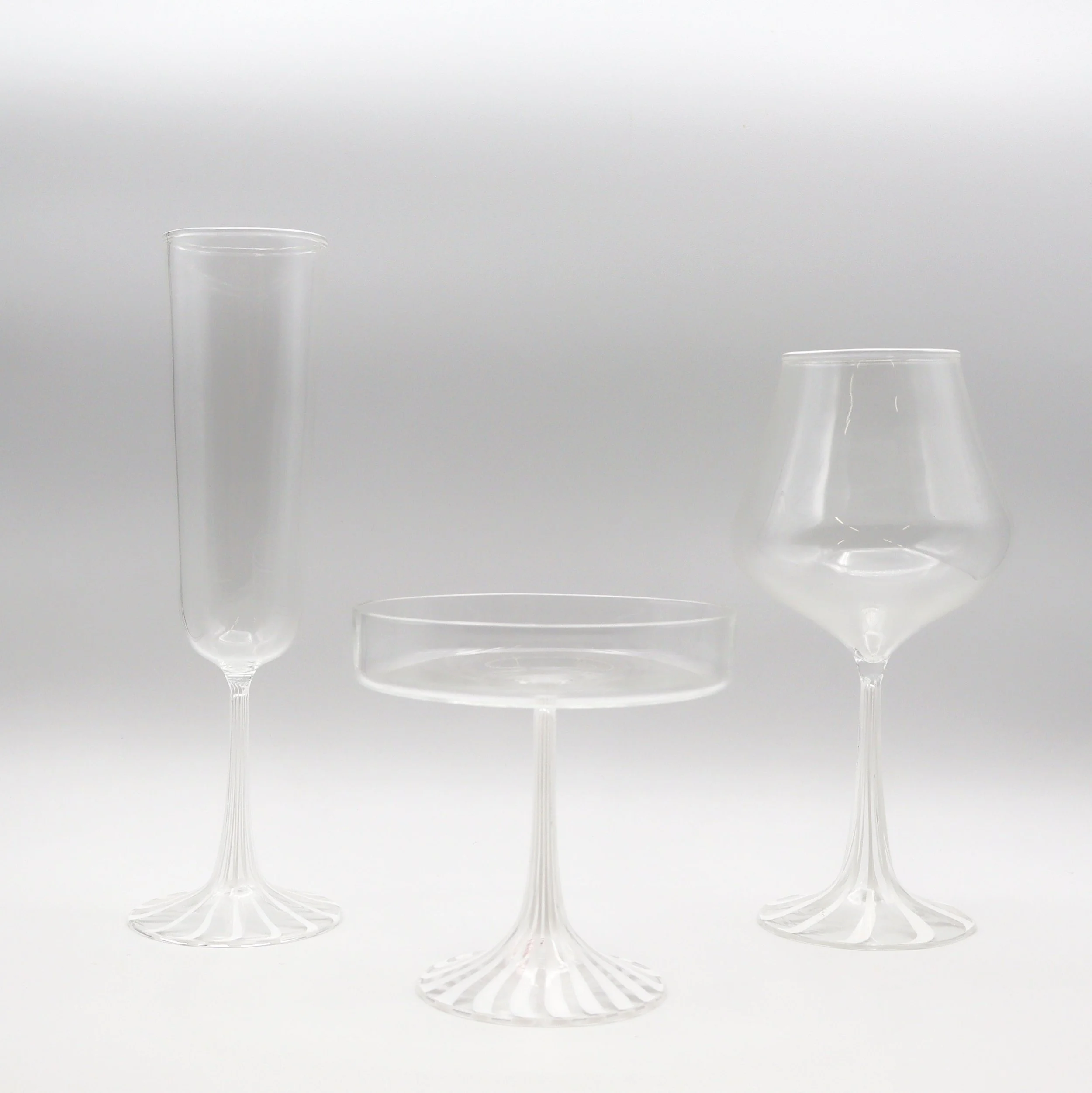 Tre bicchieri di vetro trasparente con forme diverse su uno sfondo bianco.