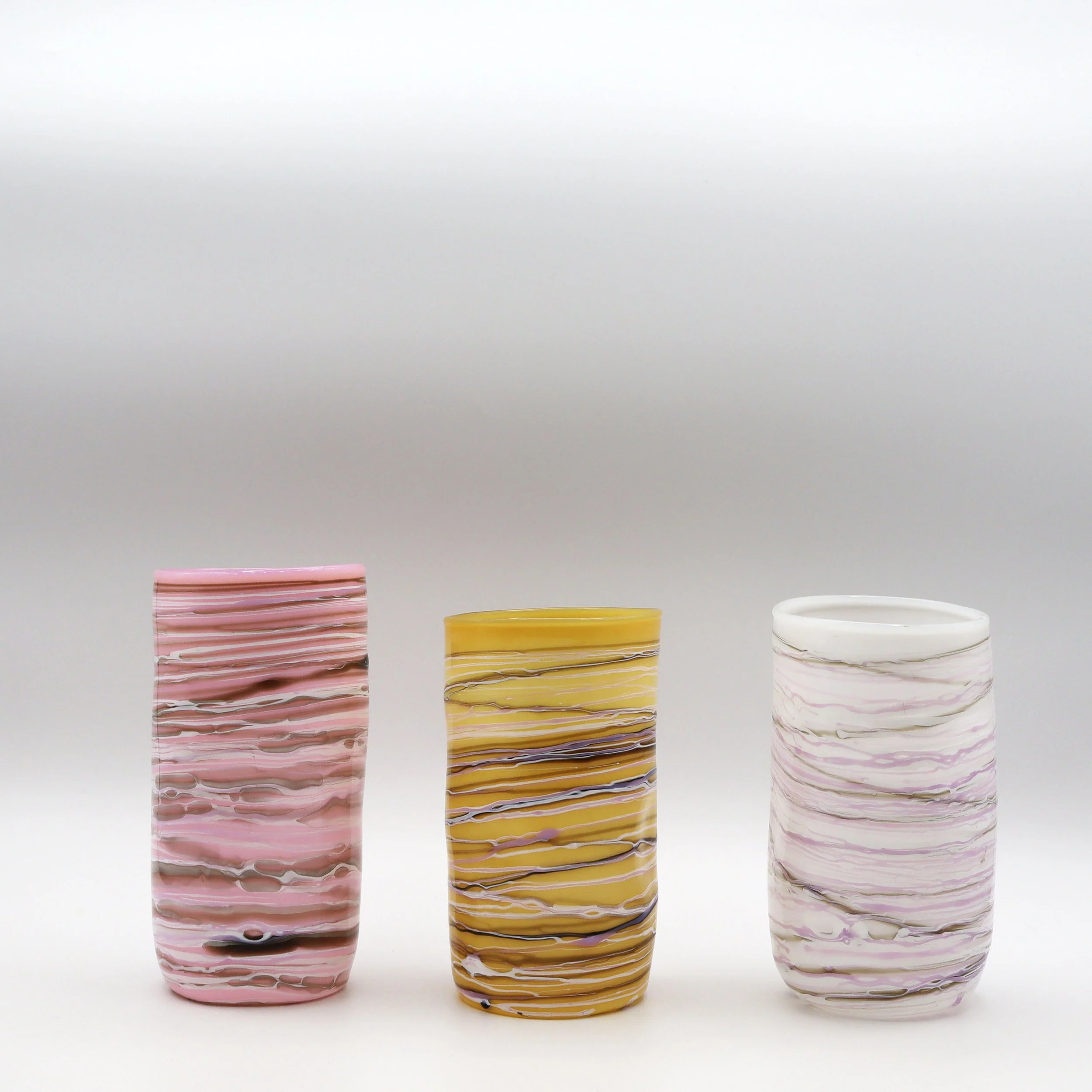 Tre bicchieri in vetro con motivi marmorizzati di colori rosa, giallo e bianco