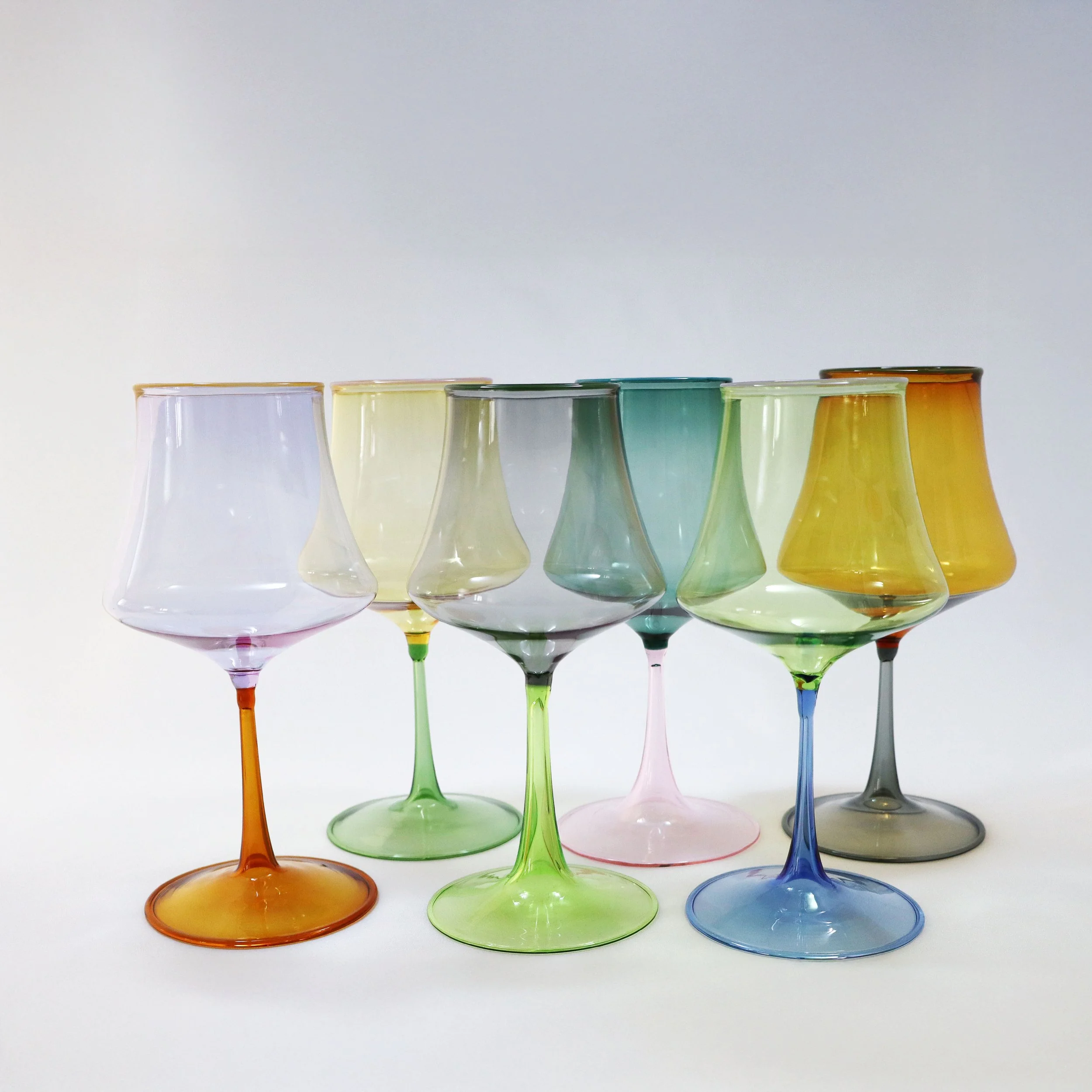 Set di otto bicchieri di vetro colorati con steli variopinti, disposti su uno sfondo bianco.