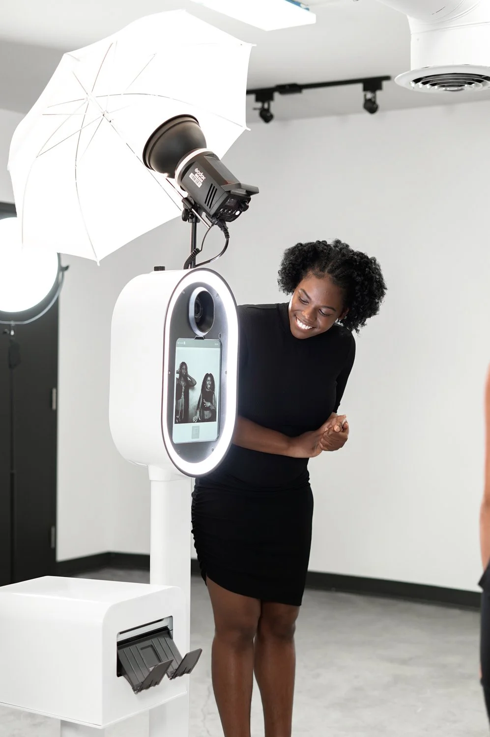 Woman in black dress smiling and posing in front of a photo booth with professional lighting equipment.