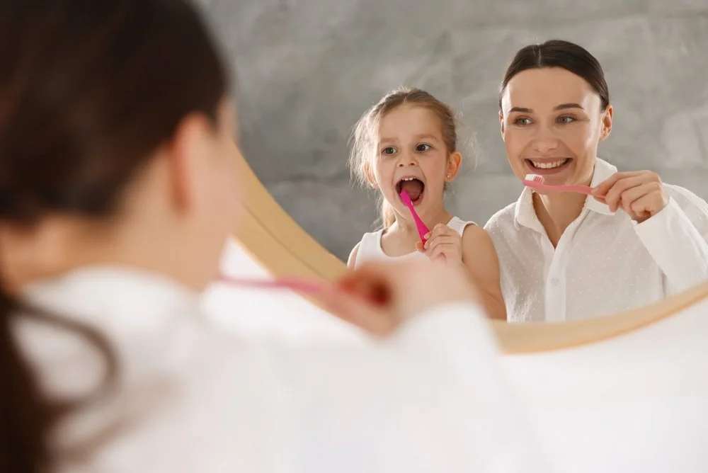 parent supervising children’s brushing habits while a child learns to brush independently