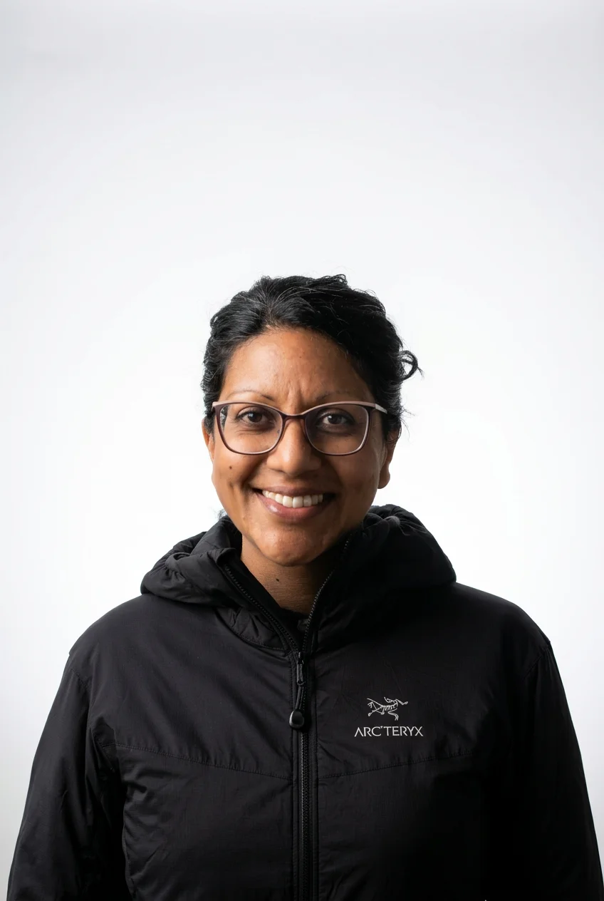 Smiling woman wearing glasses and a black Arc'teryx jacket against a white background