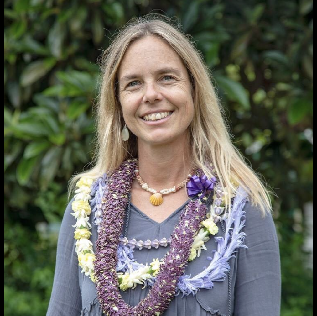 Smiling woman wearing flower leis in an outdoor setting.