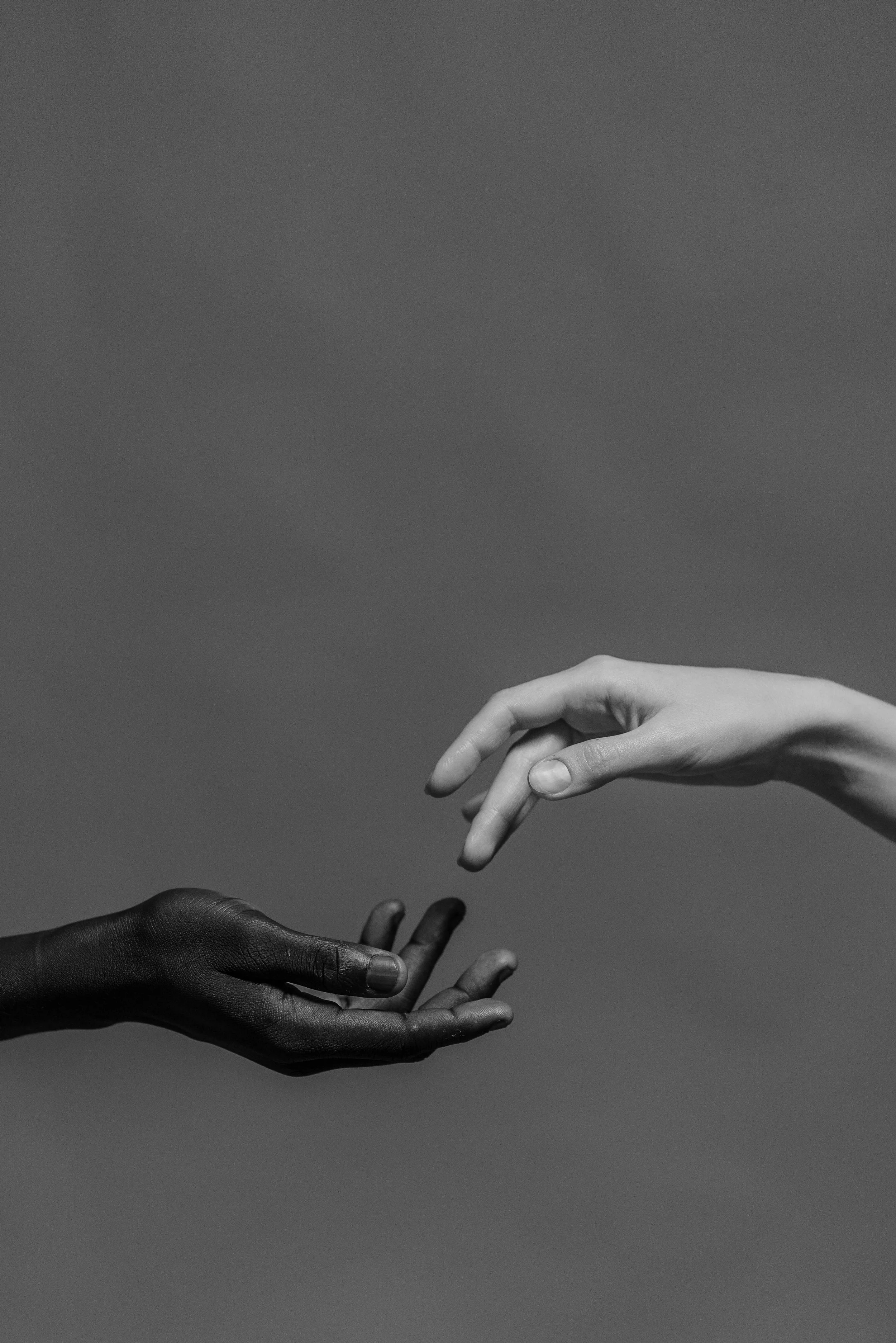 Twee handen met verschillende huidskleuren reiken naar elkaar tegen een neutrale achtergrond – symbool voor verbinding en gelijkwaardigheid.