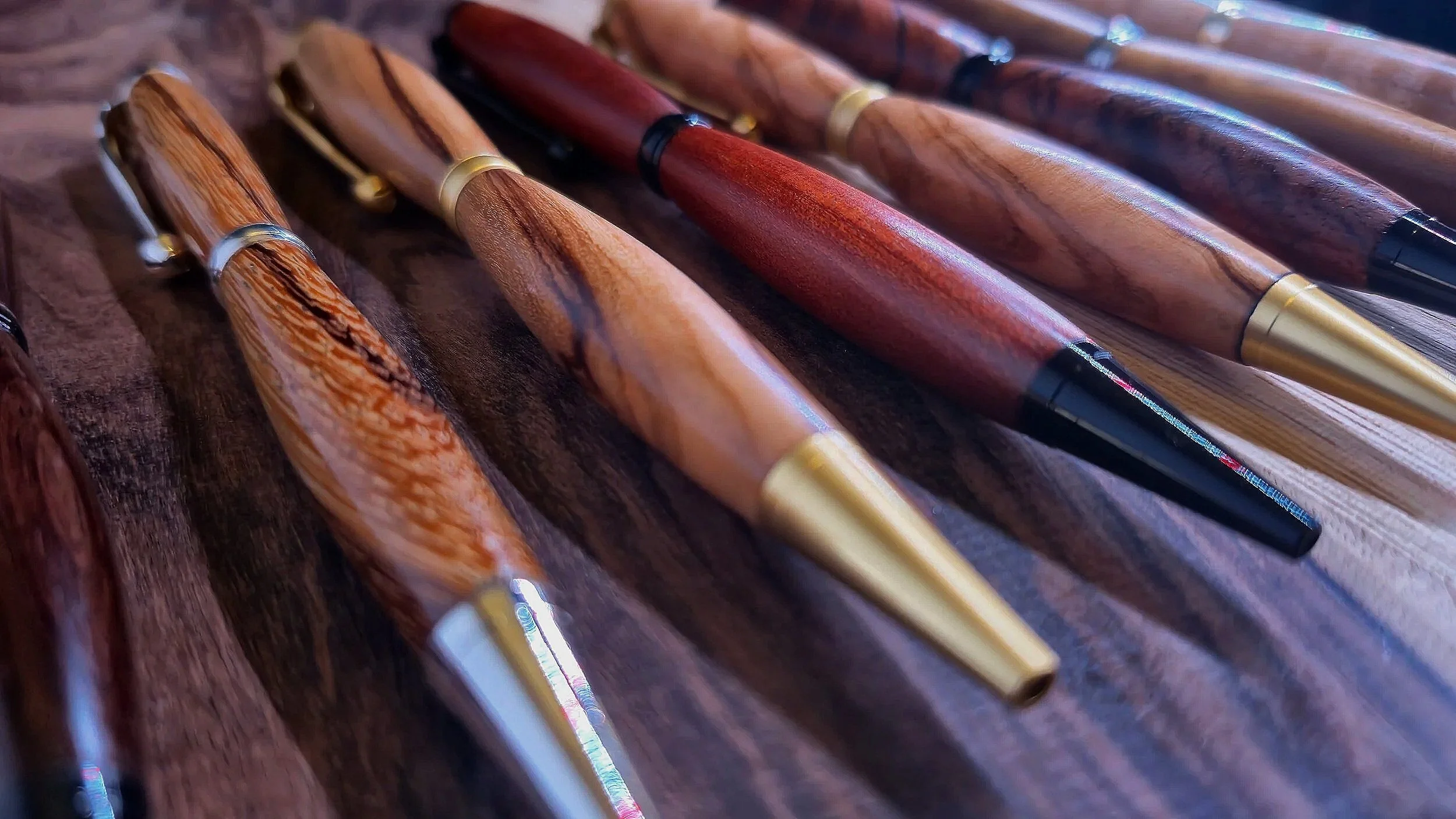 Multiple handcrafted wood pens with gold and black accents lying on a wooden surface.