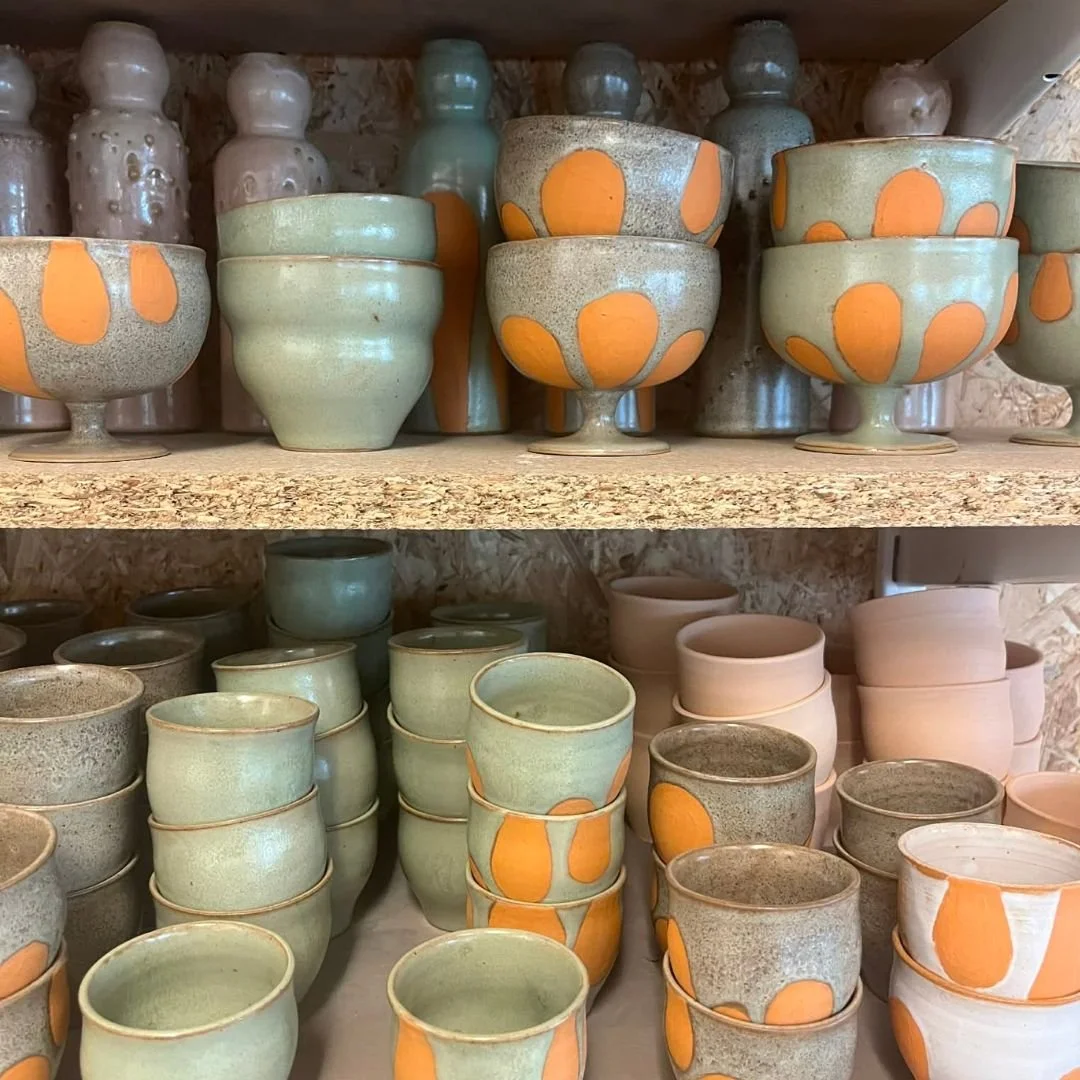Assortiment de bols et de vases en céramique, certains décorés avec des motifs orange, sur des étagères en bois.