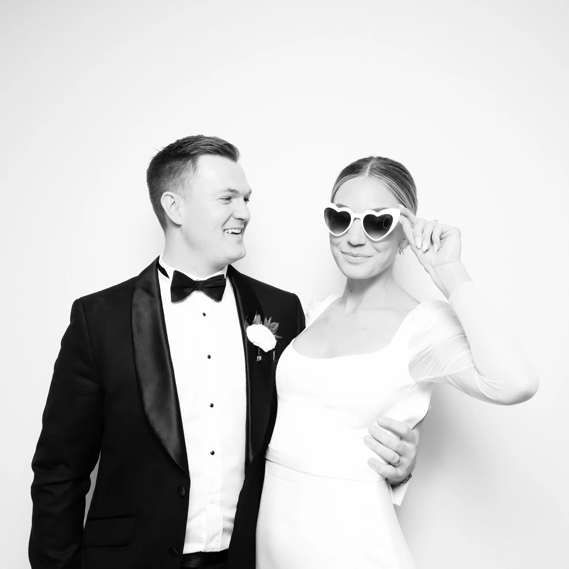 Newlyweds with heart-shaped sunglasses at black and white glam photo booth with clean backdrop