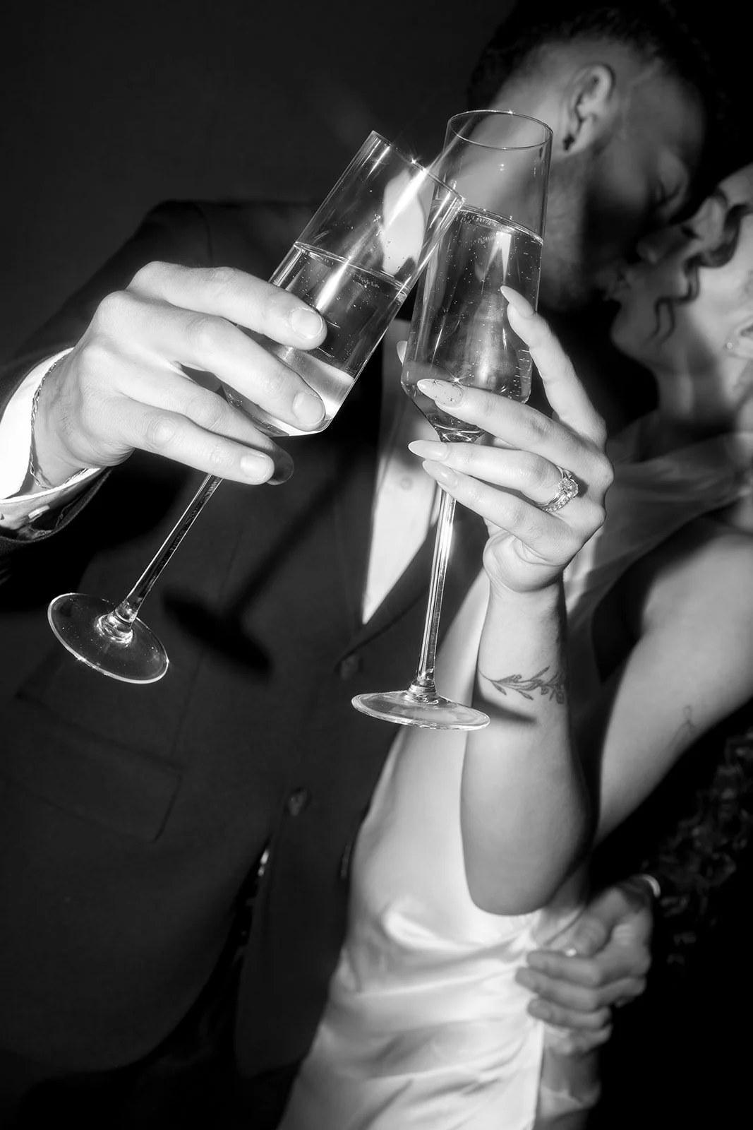 Black and white close-up of bride and groom toasting champagne showing wedding rings at glam photo booth