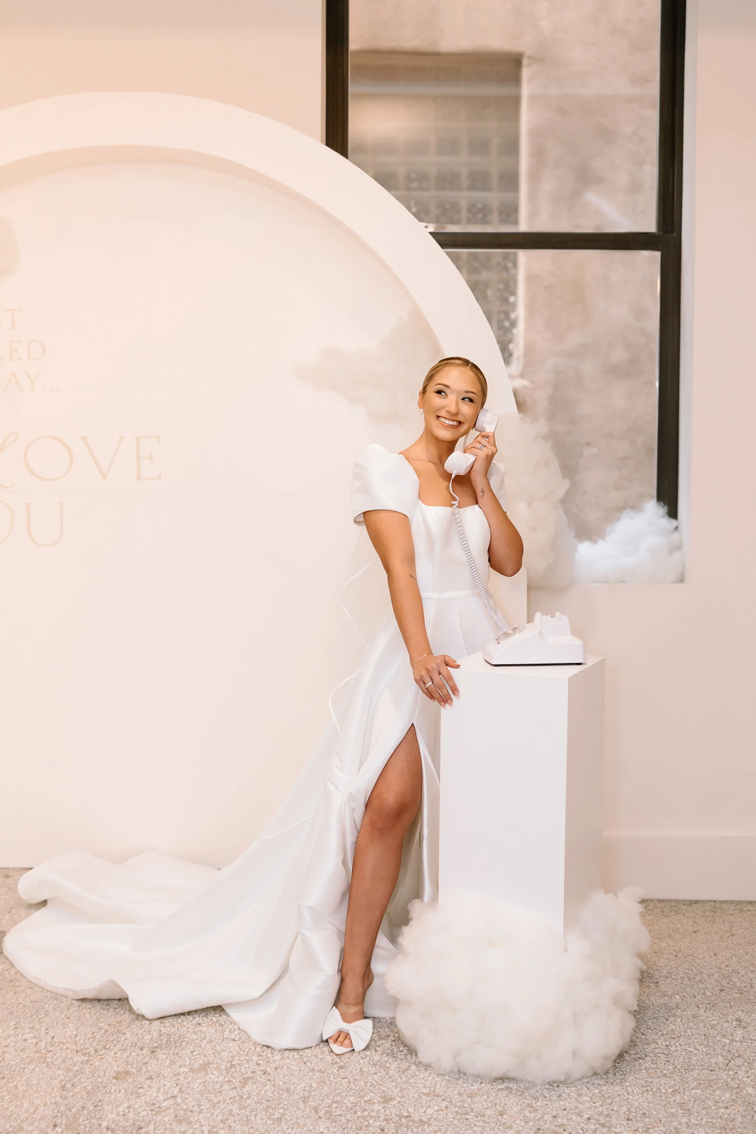 Bride in elegant white gown leaving voice message on vintage phone guest book with modern minimalist circular backdrop