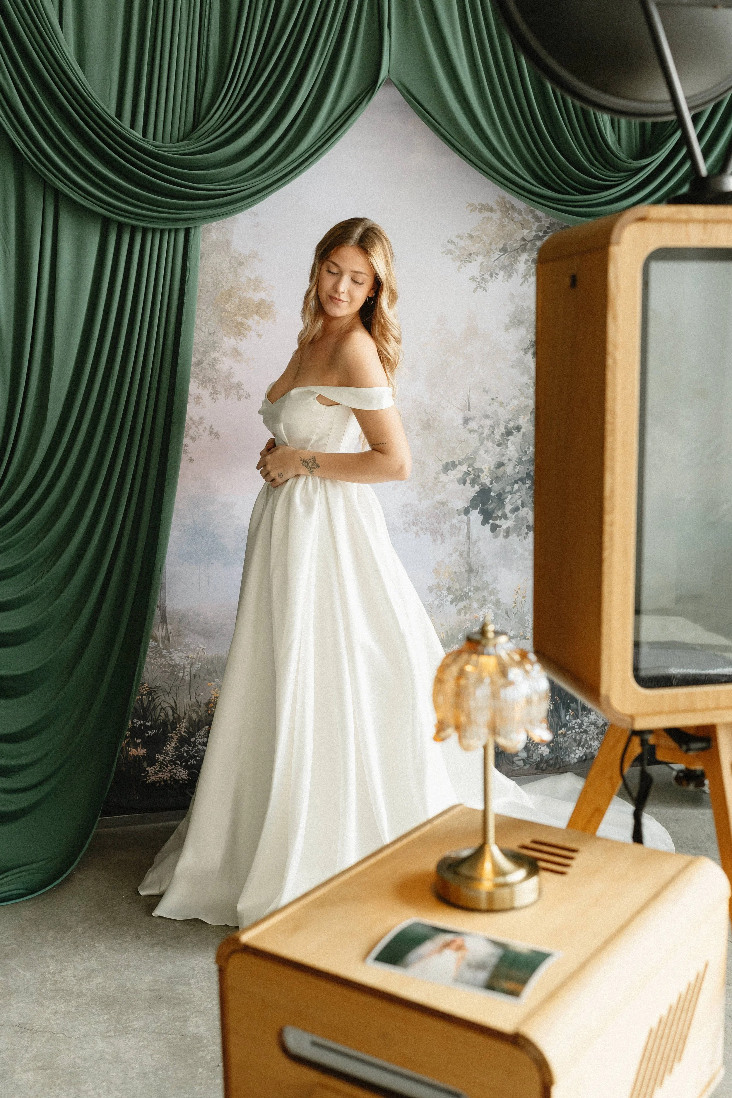 A woman in a white dress standing in front of a scenic background with greenery and trees,518x850