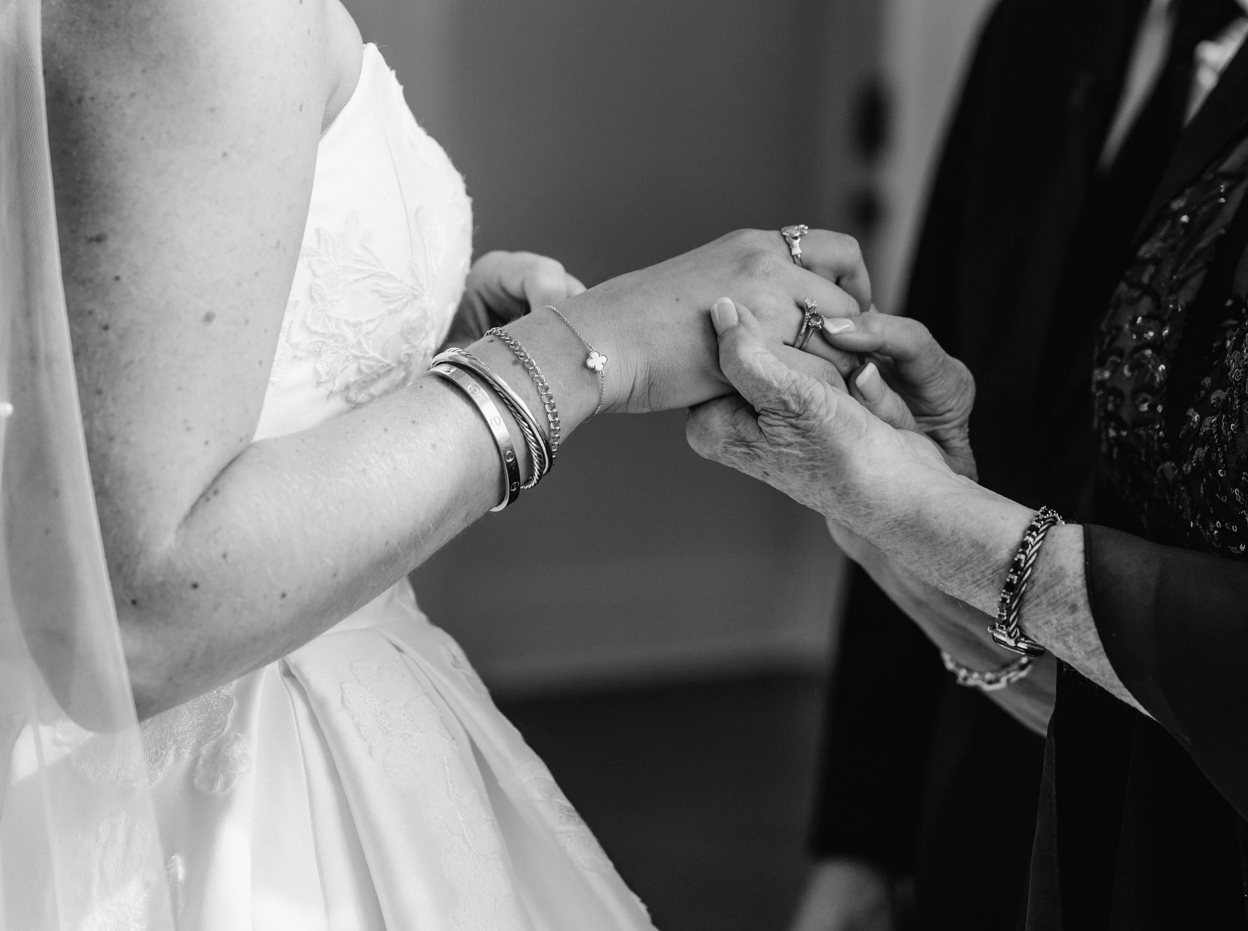 B&W close-up of bride’s hands, bracelets, lace gown detail