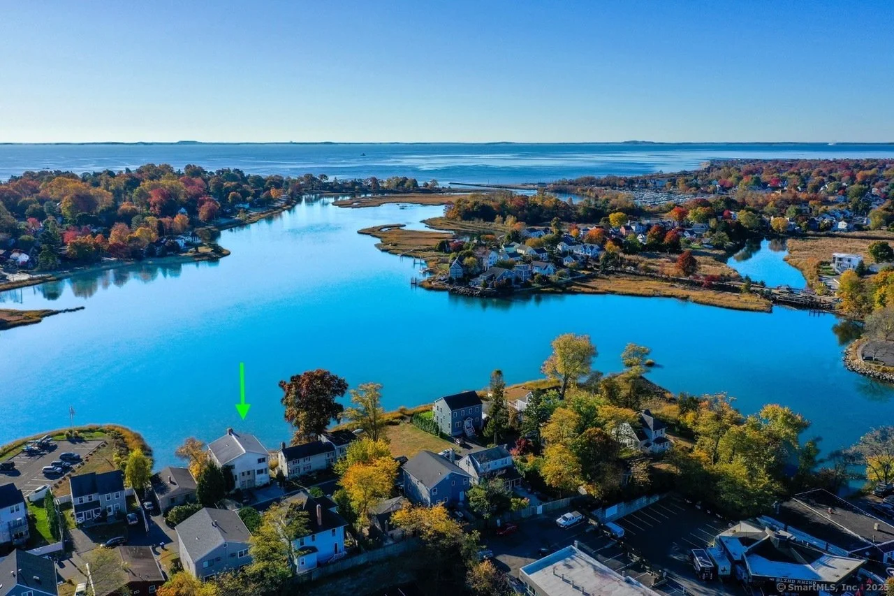 Aerial view of a coastal area with a river, houses, and autumn foliage.