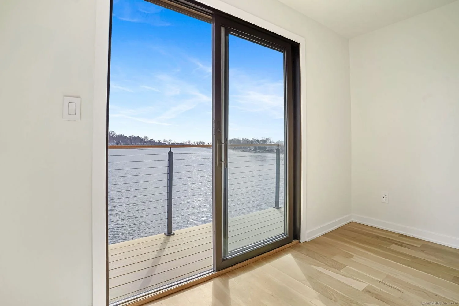 Room with glass sliding door leading to a balcony overlooking water and clear blue sky.