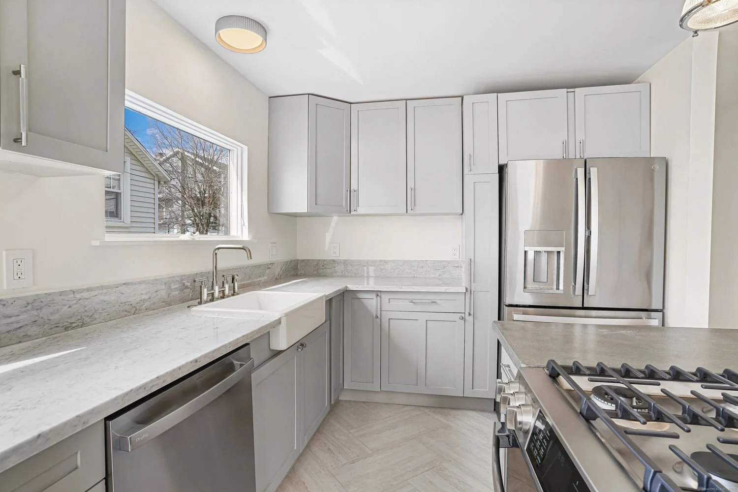 Modern kitchen with white cabinets, stainless steel appliances, farmhouse sink, and marble countertops.