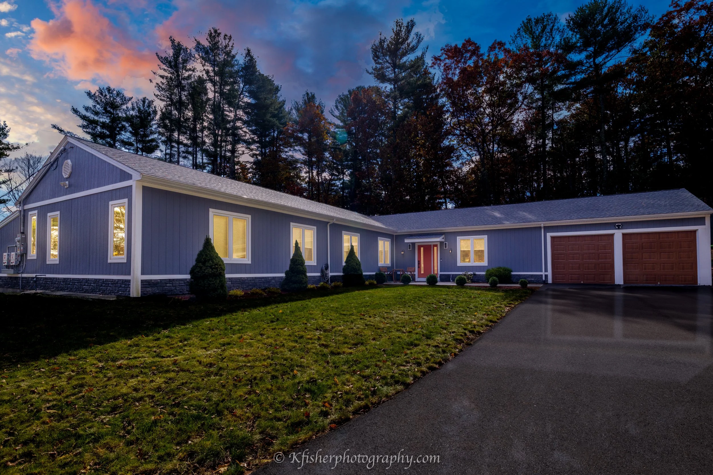 Modern two-story house with stone facade and garage, illuminated at dusk with a colorful sky in the background.