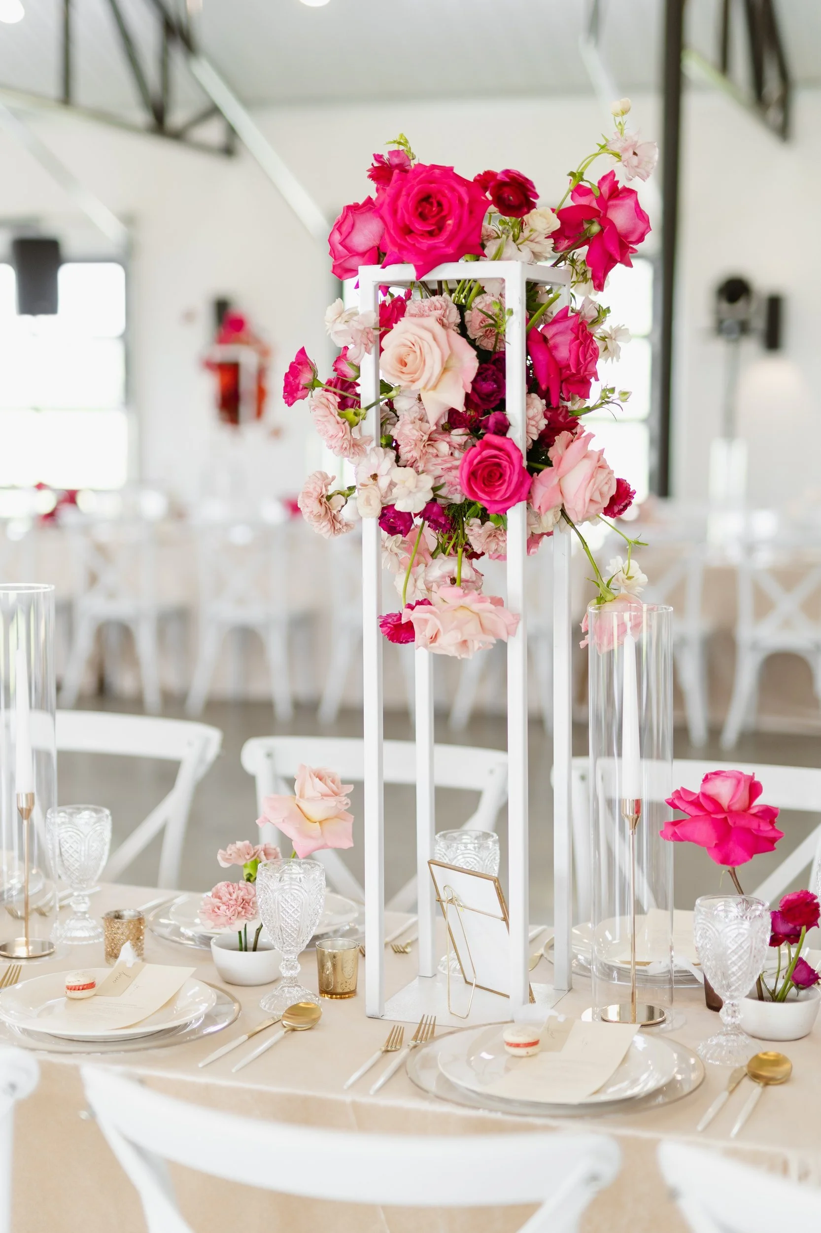 Tall clear stand topped with hot pink and red flowers above a long reception table