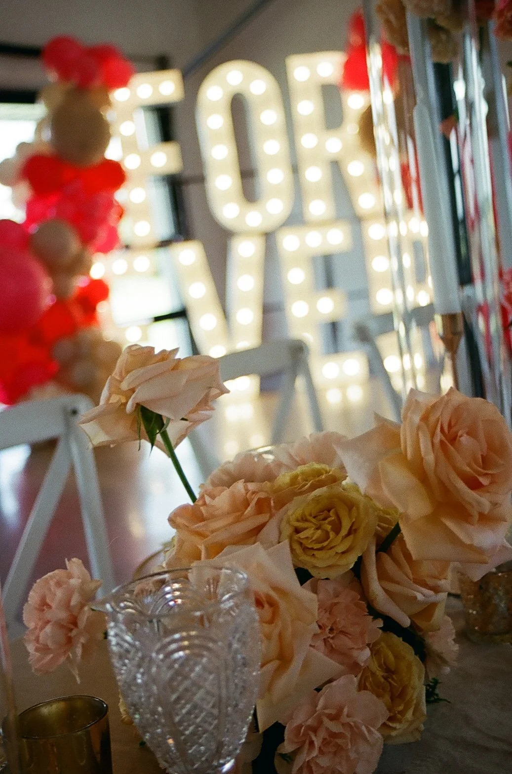 Film photo of peach and red flowers in front of lit FOREVER marquee letters