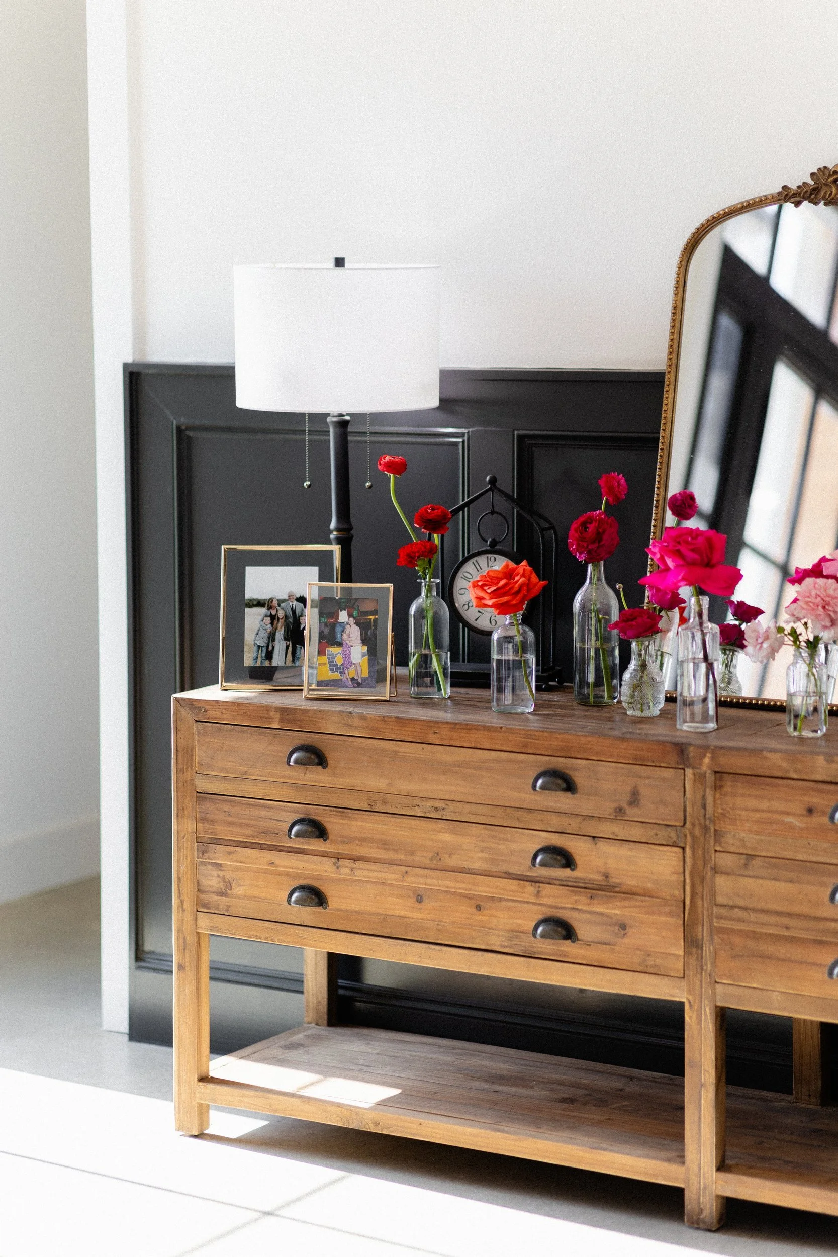 Wooden dresser with framed photos and small vases of red flowers