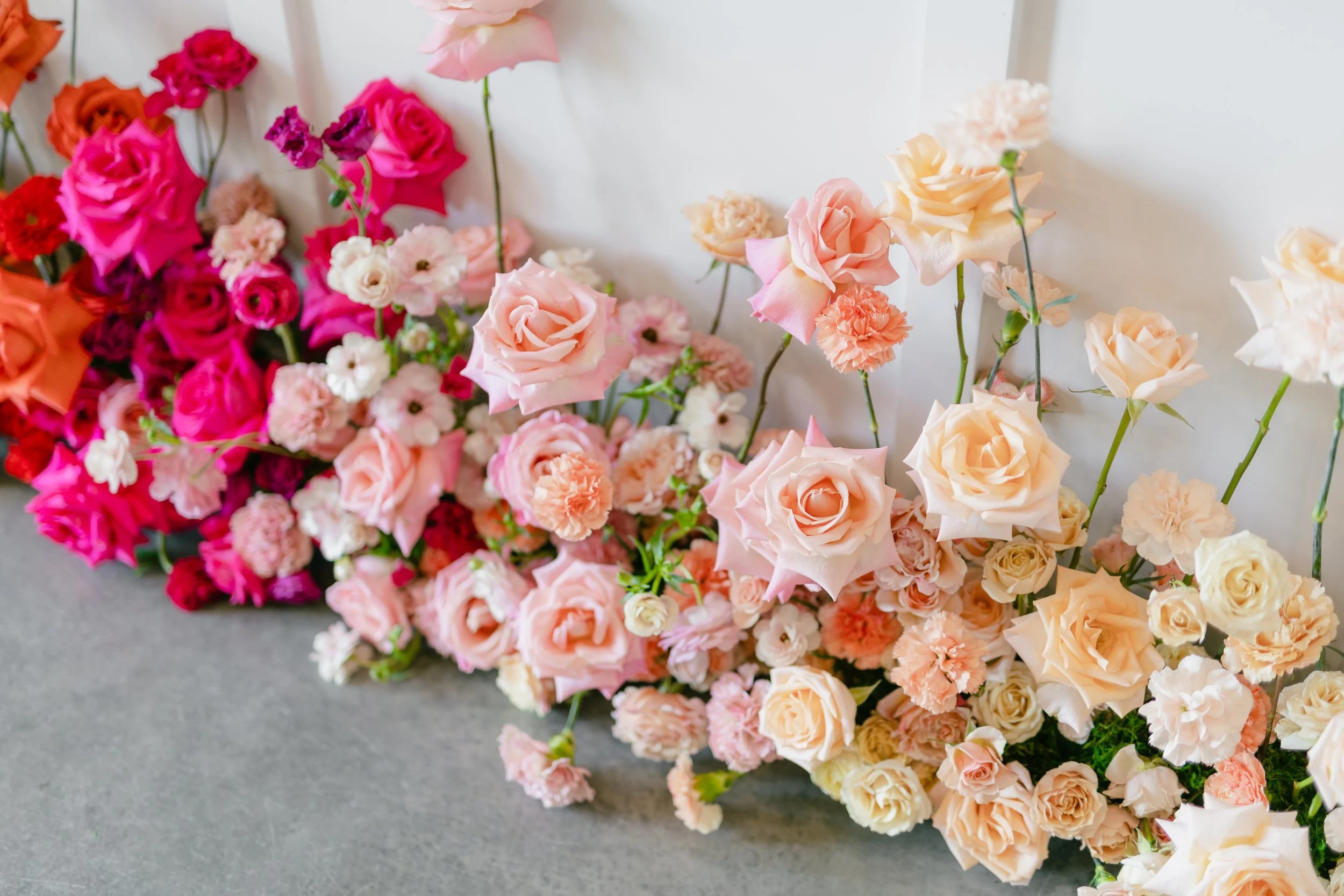 Wide floor install of hot pink, coral and peach blooms against a white wall