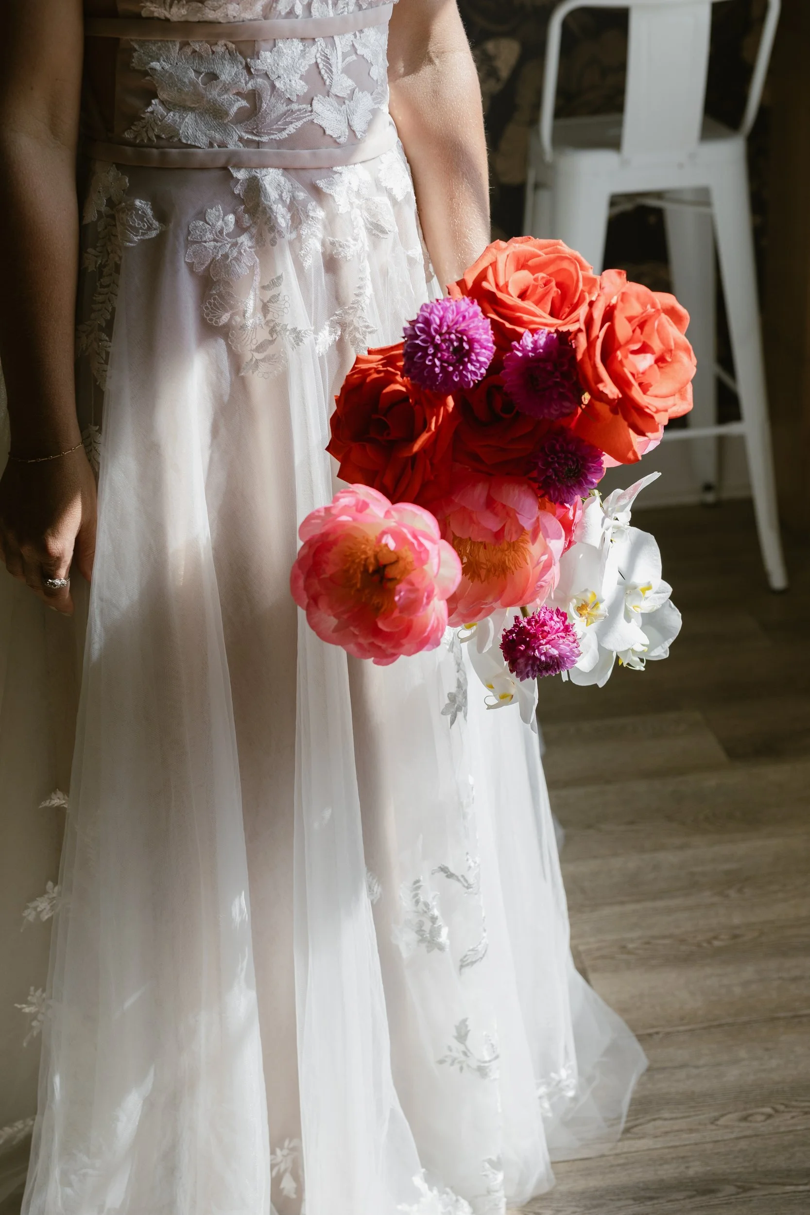 Bride holding a red, orange and purple bouquet against a lace gown