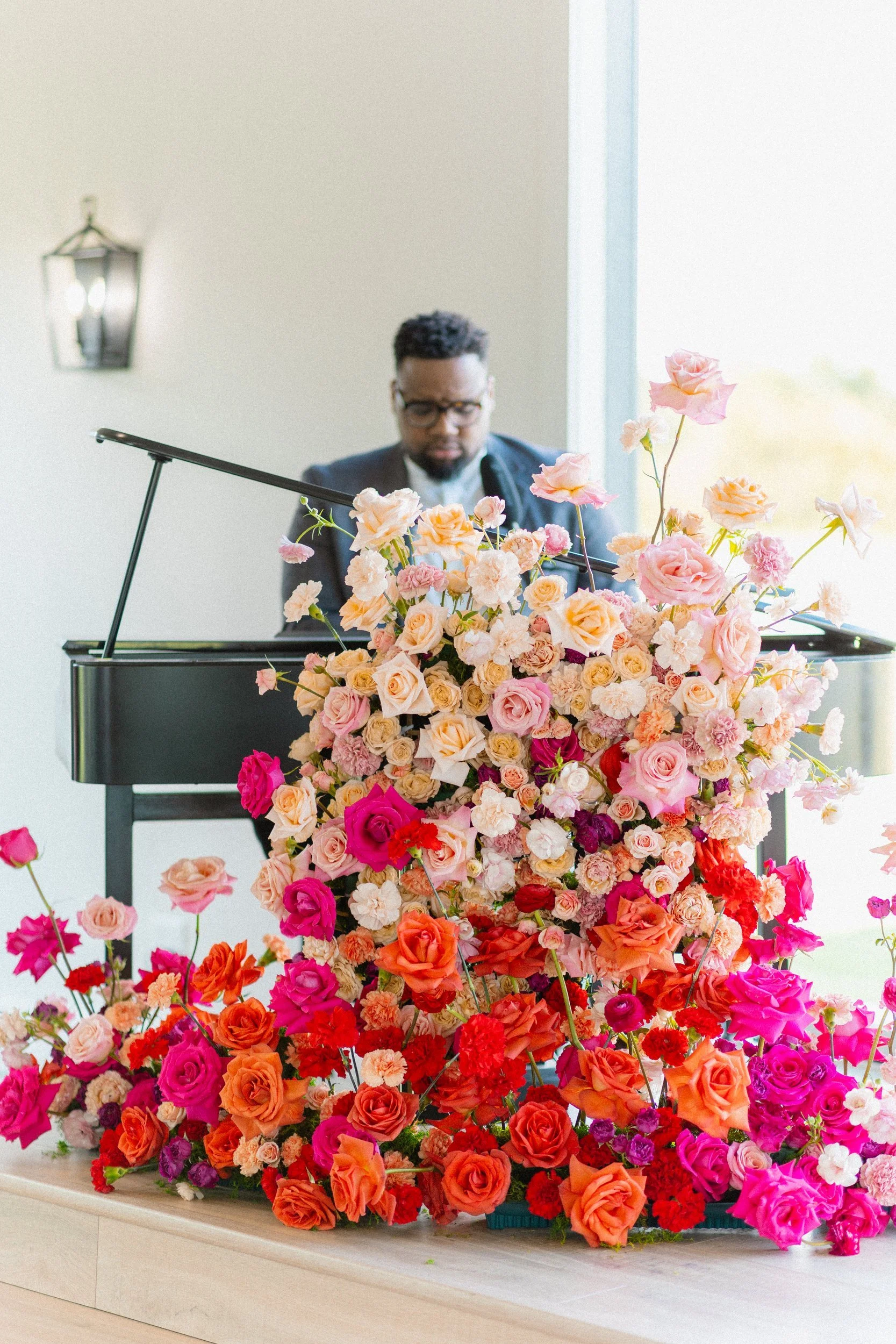 Pianist playing beside a large cascading install of orange, pink and peach roses