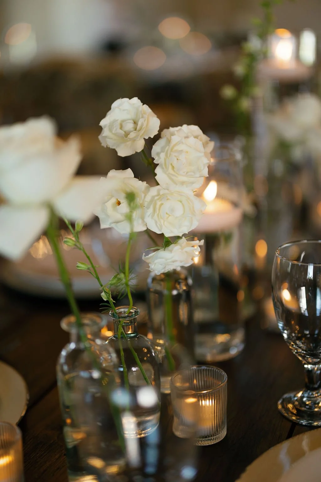 Detail of spray roses in clear bud vases, on wooden farm tables